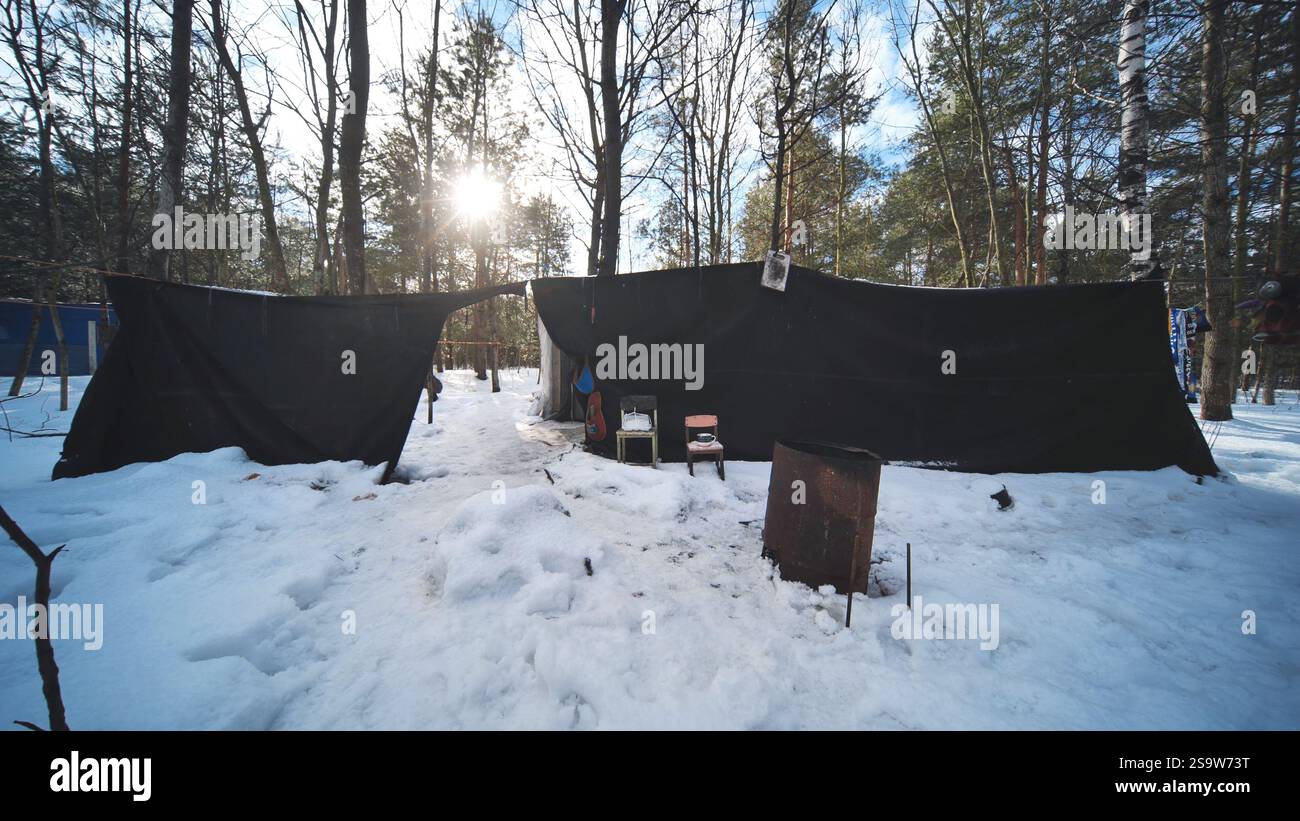 Abri de fortune fait de bâche noire dans la forêt enneigée, offrant un refuge aux sans-abri pendant l'hiver froid Banque D'Images