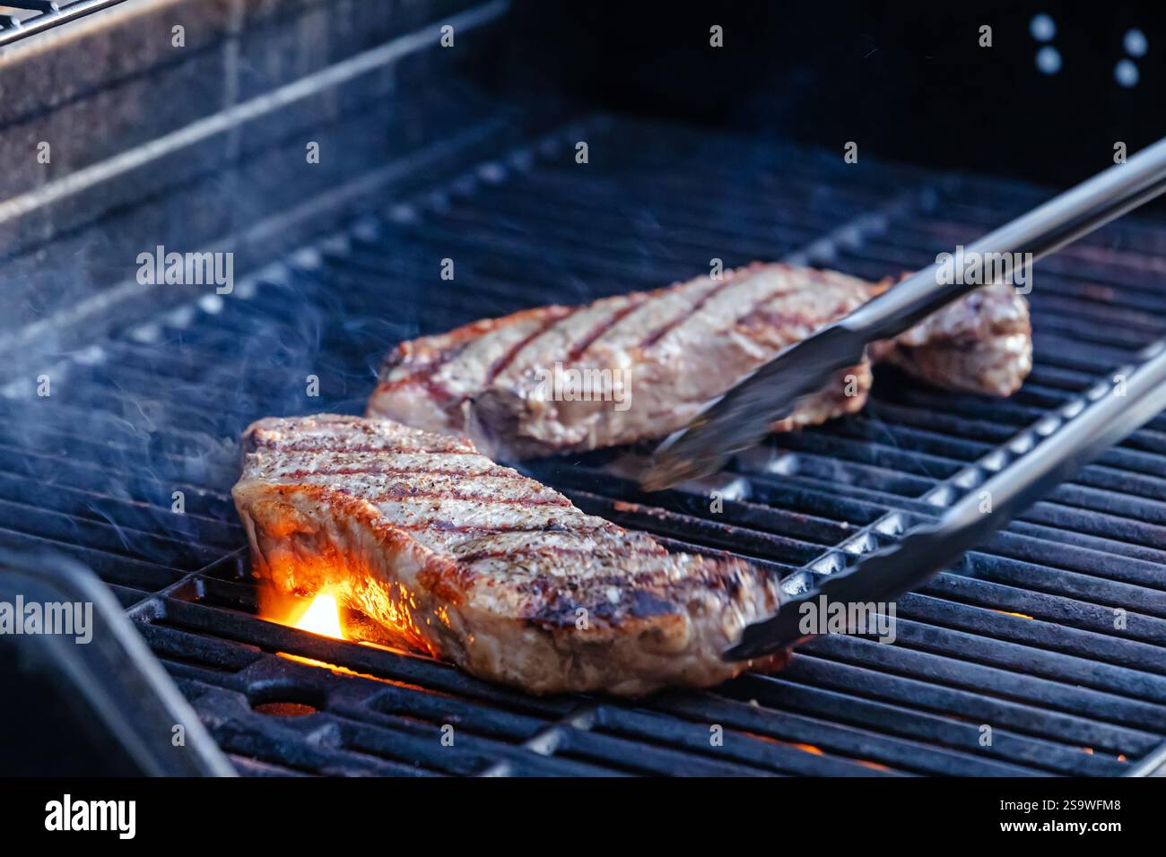 Vue rapprochée de deux steaks juteux grésillant sur le grill extérieur chaud Banque D'Images