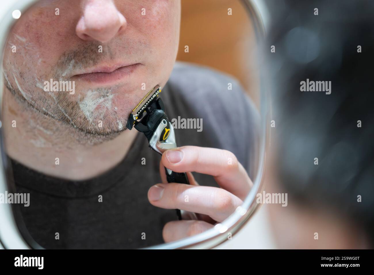 Homme d'âge moyen regardant dans un miroir extensible fixé au mur et se rasant à l'aide d'un rasoir de sécurité Gillette, Royaume-Uni. Concept : toilettage personnel, routine matinale Banque D'Images