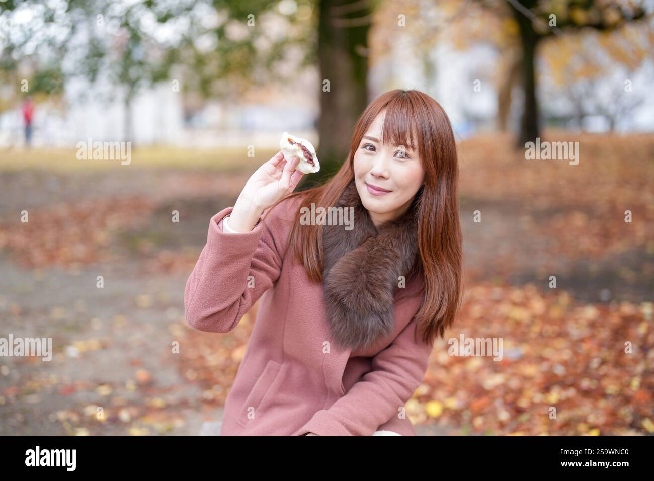 Un parc avec de belles feuilles d'automne. Les femmes japonaises aux cheveux longs dans la trentaine mangent des brioches à la viande. Banque D'Images