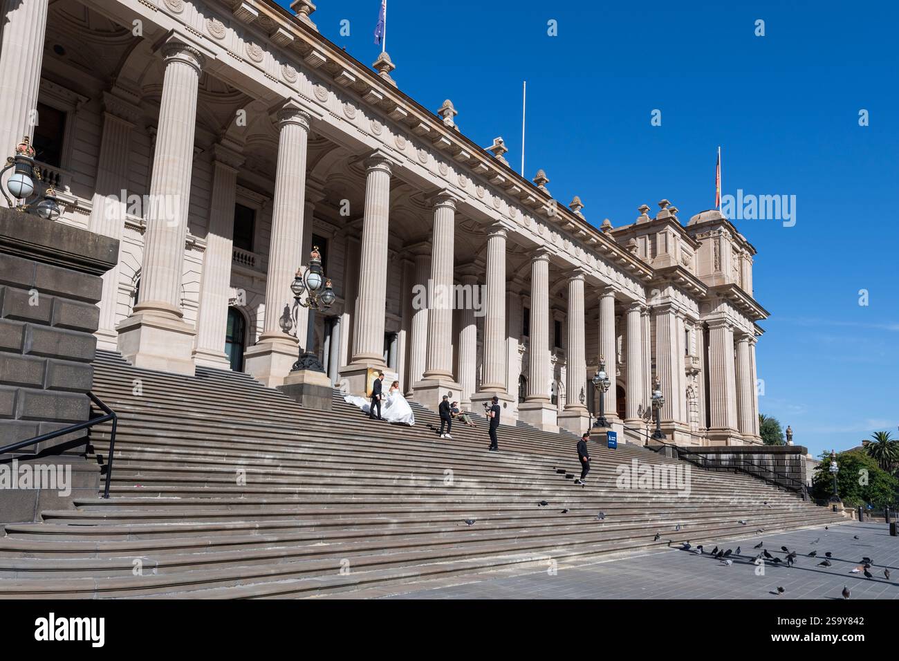 Une mariée en robe blanche et le marié ont leurs photos de mariage sur les marches du Parlement lors d'une journée ensoleillée sous le ciel bleu à Melbourne en Australie Banque D'Images