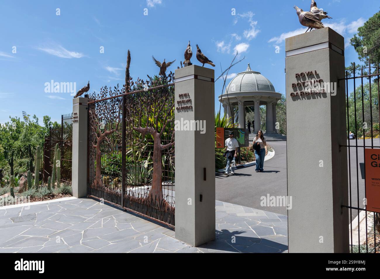 Un couple indien se promène vers les portes de fer ornées de sculptures de pie au sommet des poteaux de porte à l'entrée des jardins botaniques royaux de Melbourne, Australie Banque D'Images