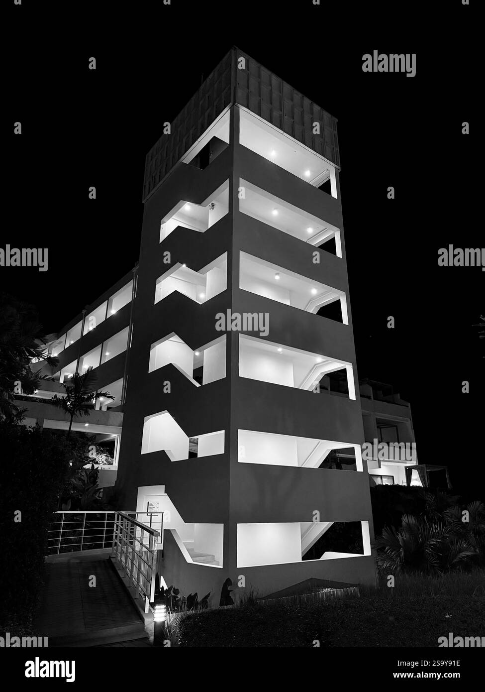 Bâtiment moderne la nuit Une vue en angle bas d'un bâtiment moderne avec des motifs géométriques et des lumières vives, capturée la nuit en noir et blanc. - Image de stock capturée avec un smartphone