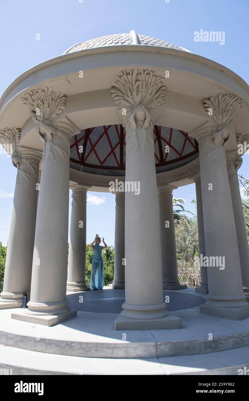 Une fille asiatique dans une robe bleue rétro-éclairée par le soleil prend un selfie entre des colonnes cannelées dans le Temple du vent, Royal Botanic Gardens, Melbourne Banque D'Images