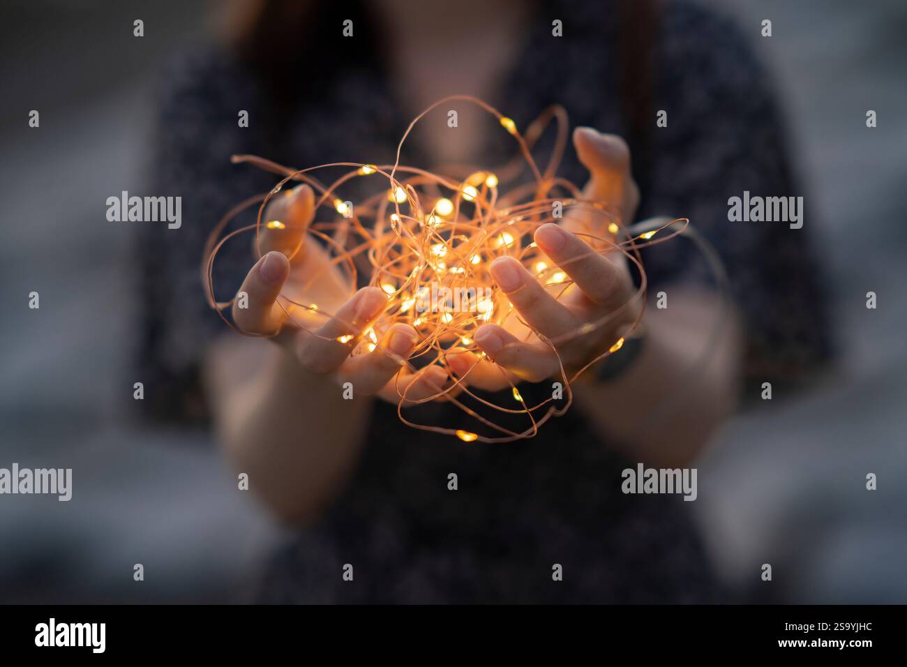 Jeune femme enroulant ses mains autour d'une lumière éclairée Banque D'Images