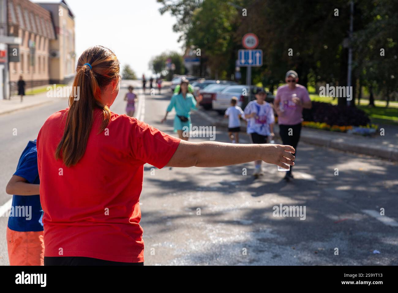 Un volontaire portant un t-shirt rouge tient une tasse d'eau en plastique à un coureur de marathon. L'image capture l'esprit de soutien et de communauté à un sport Banque D'Images