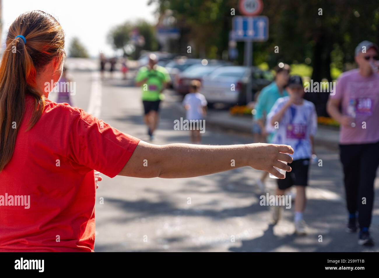 Un volontaire portant un t-shirt rouge tient une tasse d'eau en plastique à un coureur de marathon. L'image capture l'esprit de soutien et de communauté à un sport Banque D'Images