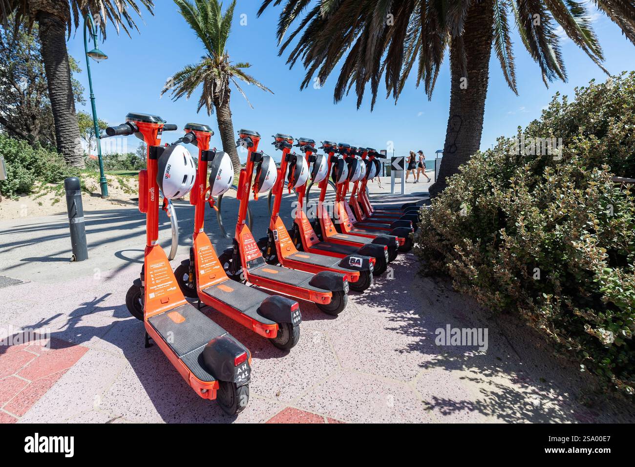 Un groupe de scooters électriques oranges avec des casques blancs à louer alignés dans une rangée à Melbourne. Concept : rechargeable, commodité, mobilité Banque D'Images