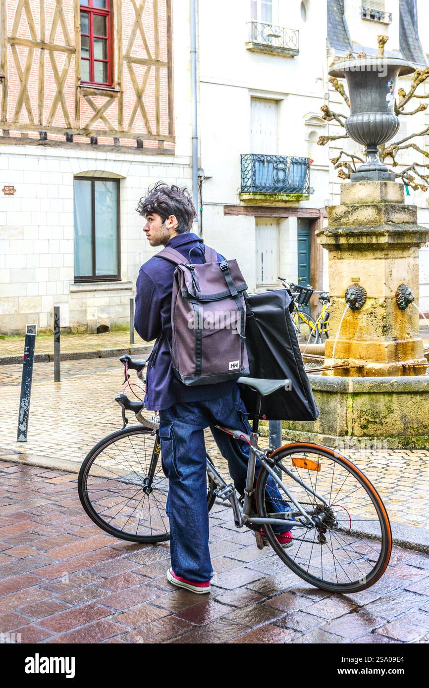 Jeune étudiant masculin avec sac à dos et portfolio arrêté à vélo look,ing Around - Tours, Indre-et-Loire (37), France. Banque D'Images
