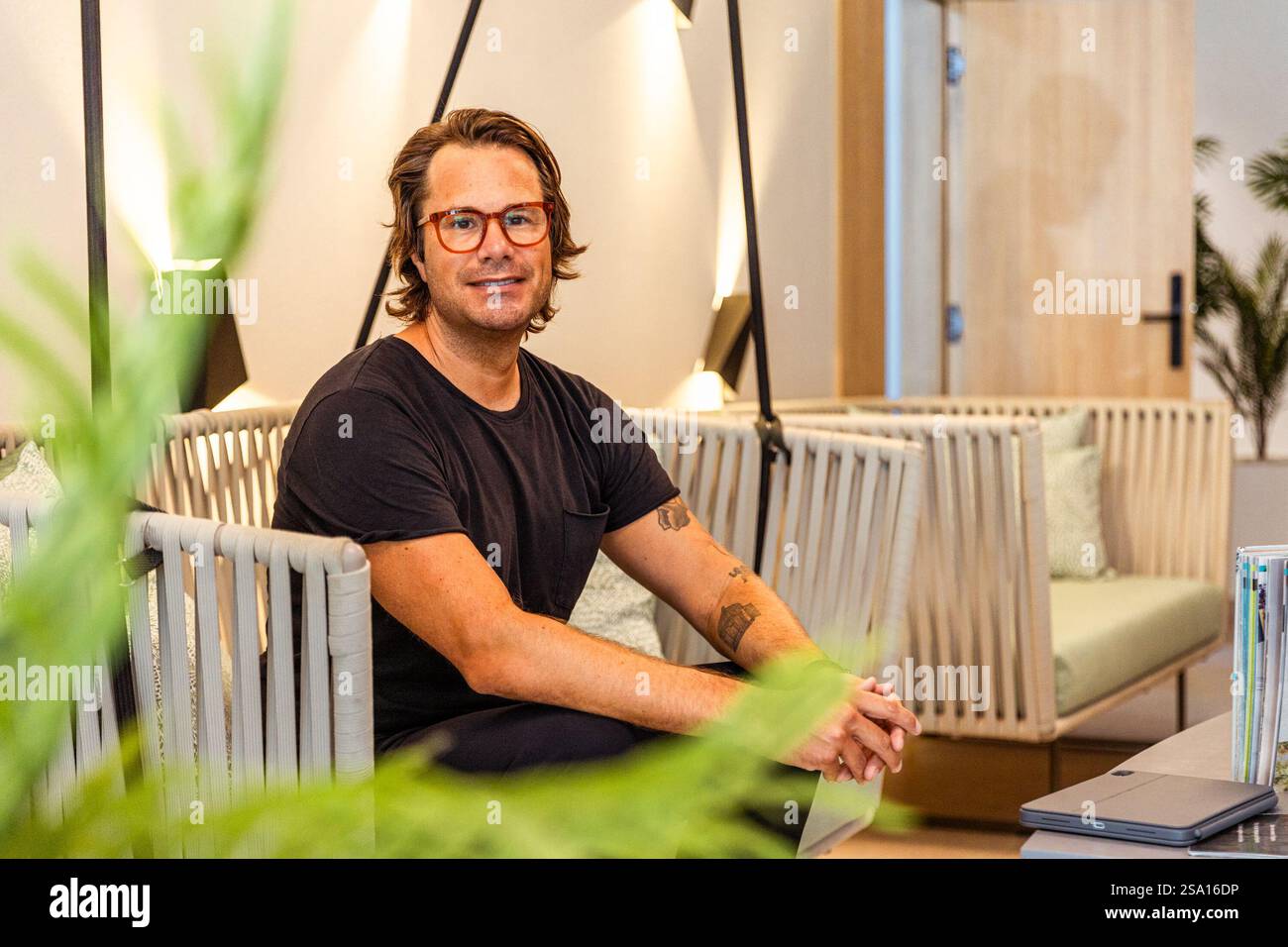 Un homme hipster dans une chemise noire portant des lunettes est assis dans une chaise, photo avec espace de copie. Banque D'Images