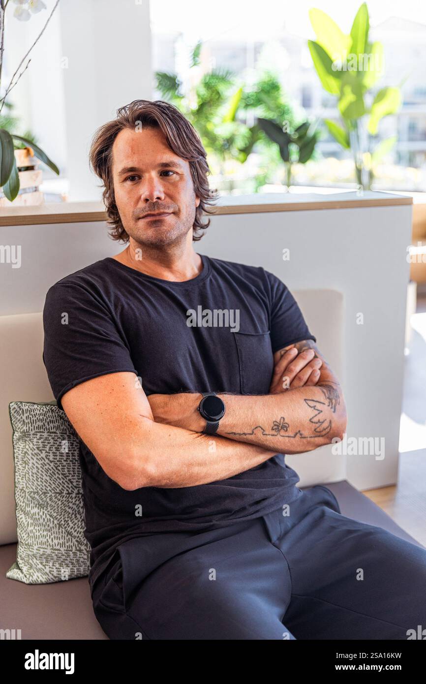 Un homme avec une montre au poignet est assis sur un canapé les bras croisés, photo avec espace copie. Concept de détente et de confort Banque D'Images