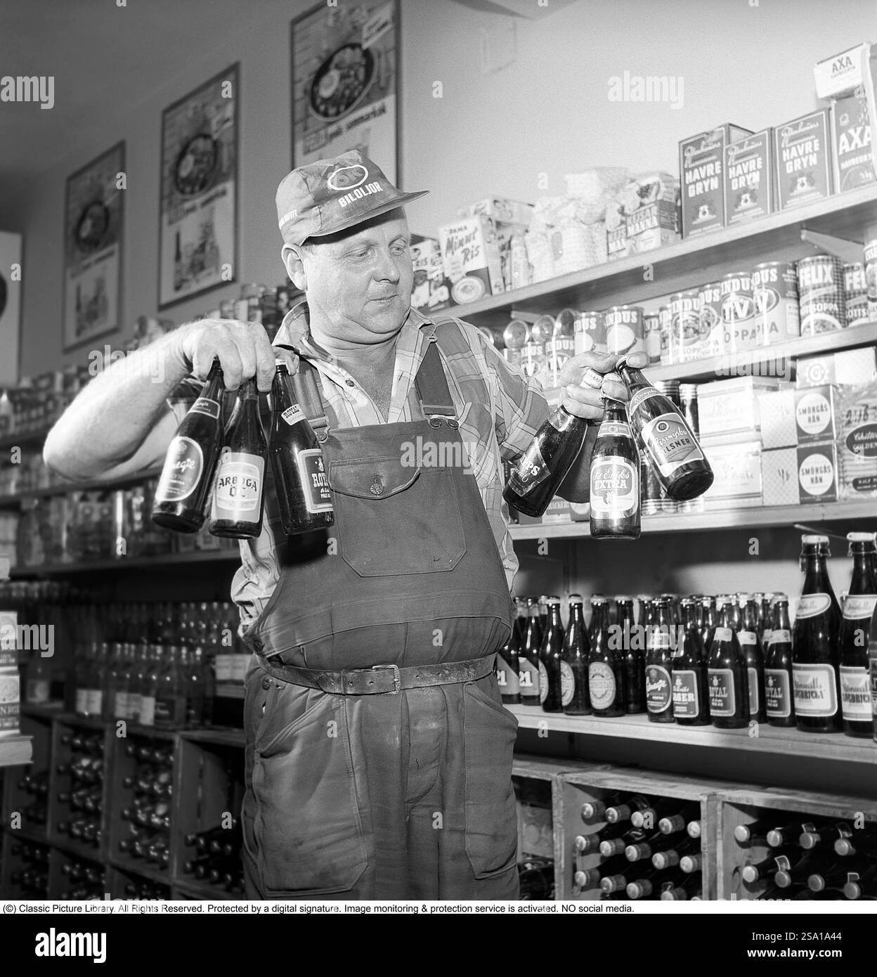 Grand choix de bières et lager en 1960. Un homme avec une bonne prise en main parvient à tenir six bouteilles de bière dans les deux mains en même temps. Des marques de bière célèbres à l'époque telles que Carnegie, Arboga Beer, Stockholms bryggerier, Pripps Special, St Eriks Extra et Risingsbo Pilsner. Il est debout dans ses vêtements de travail avec un bouchon sur qui a la chaîne d'essence OK biloljor dans le texte. En arrière-plan, vous pouvez voir qu'il est debout dans une petite épicerie avec toutes sortes d'aliments différents visibles sur les étagères. Suède 1960. Conard ref 4269 Banque D'Images