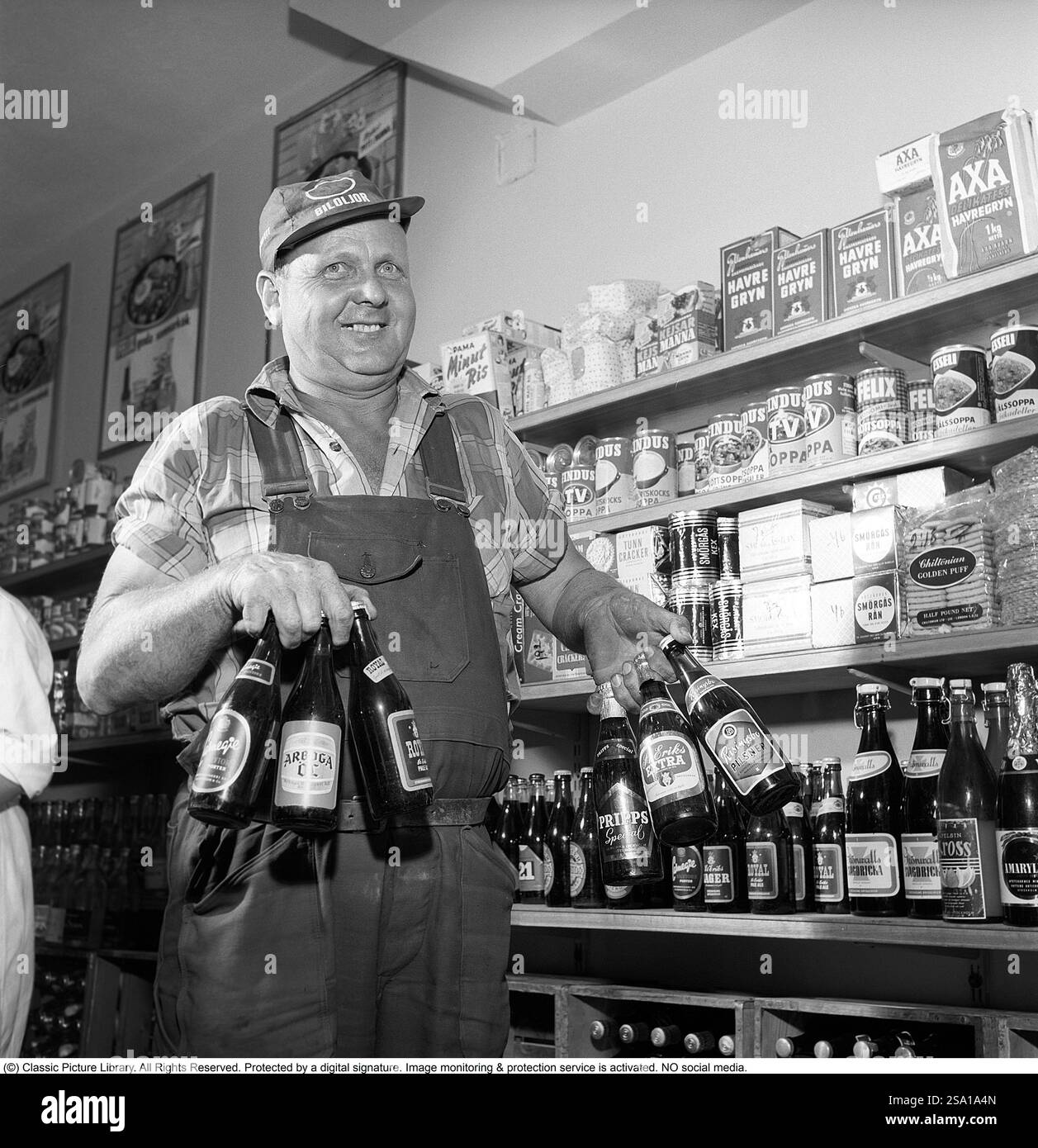 Grand choix de bières et lager en 1960. Un homme avec une bonne prise en main parvient à tenir six bouteilles de bière dans les deux mains en même temps. Des marques de bière célèbres à l'époque telles que Carnegie, Arboga Beer, Stockholms bryggerier, Pripps Special, St Eriks Extra et Risingsbo Pilsner. Il est debout dans ses vêtements de travail avec un bouchon sur qui a la chaîne d'essence OK biloljor dans le texte. En arrière-plan, vous pouvez voir qu'il est debout dans une petite épicerie avec toutes sortes d'aliments différents visibles sur les étagères. Suède 1960. Conard ref 4269 Banque D'Images