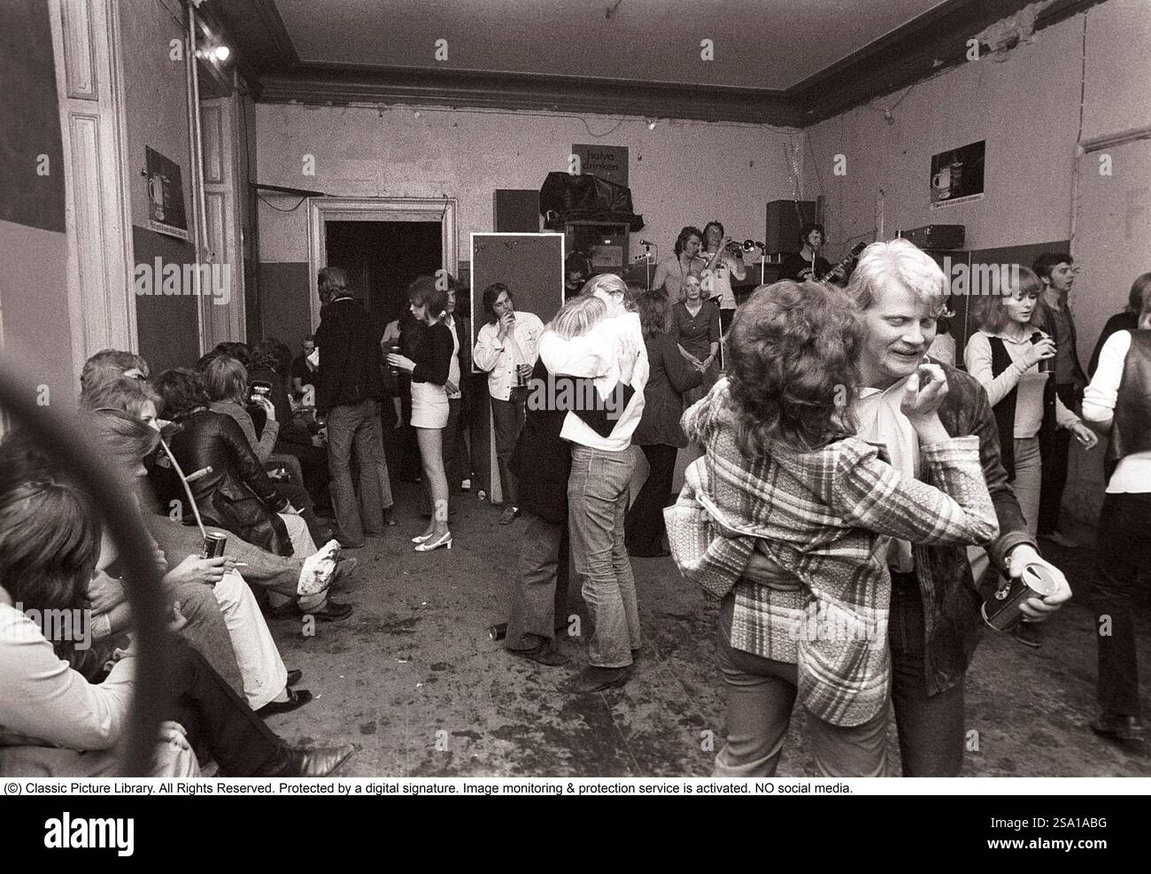 C'est ainsi que les gens faisaient la fête dans les années 1970 Les gens dansent et boivent de la bière pendant qu'un groupe joue de la musique live. Les femmes et les hommes dansent au son de la musique, boivent de la bière et fument dans une salle de fête plutôt terne que tout le monde semble apprécier et s'amuser. 1970. Kristoffersson ref 4-106-107 Banque D'Images