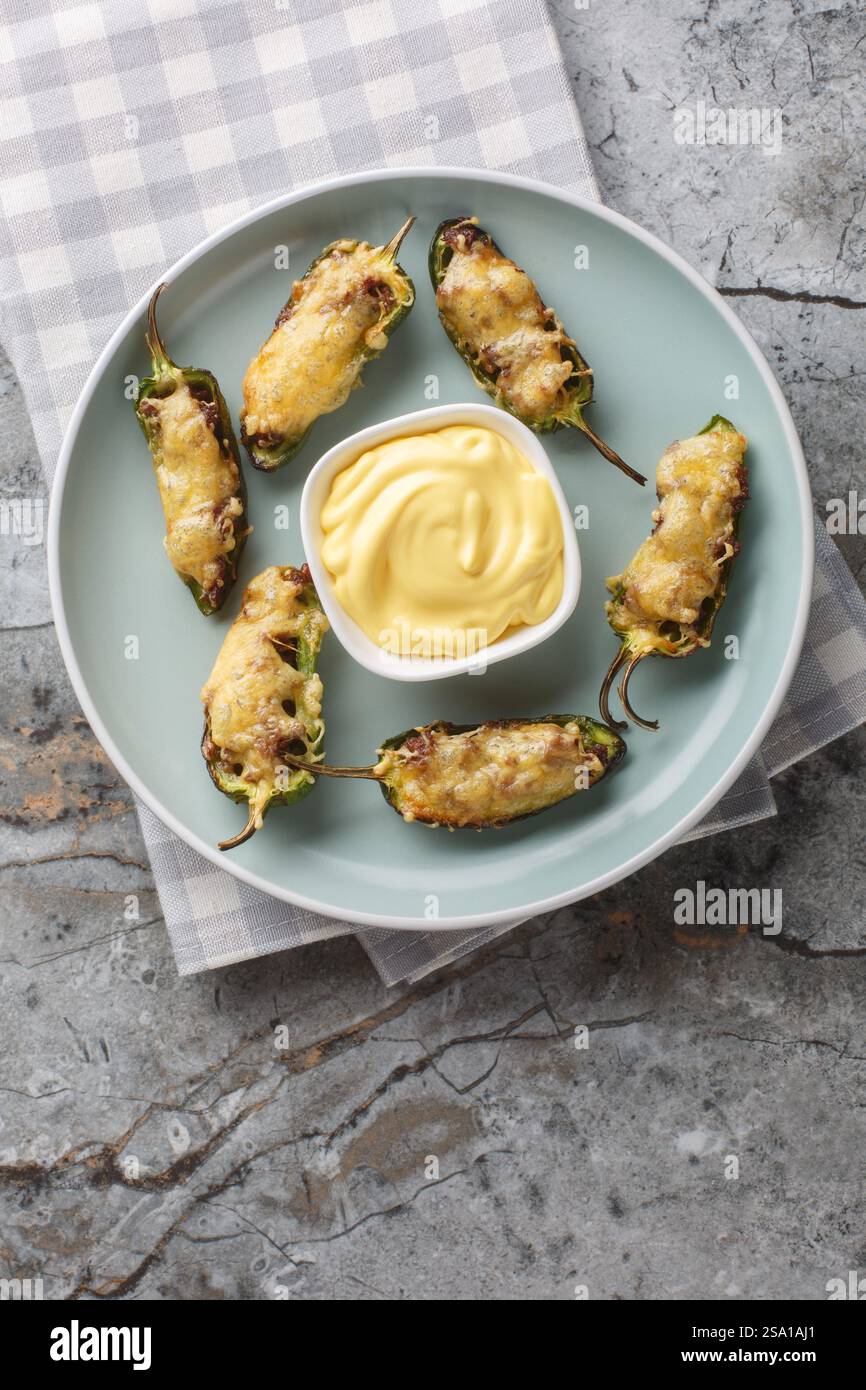 Poivrons jalapeno cuits au four avec bœuf haché et fromage servis avec une sauce gros plan dans une assiette sur la table. Vue de dessus verticale Banque D'Images