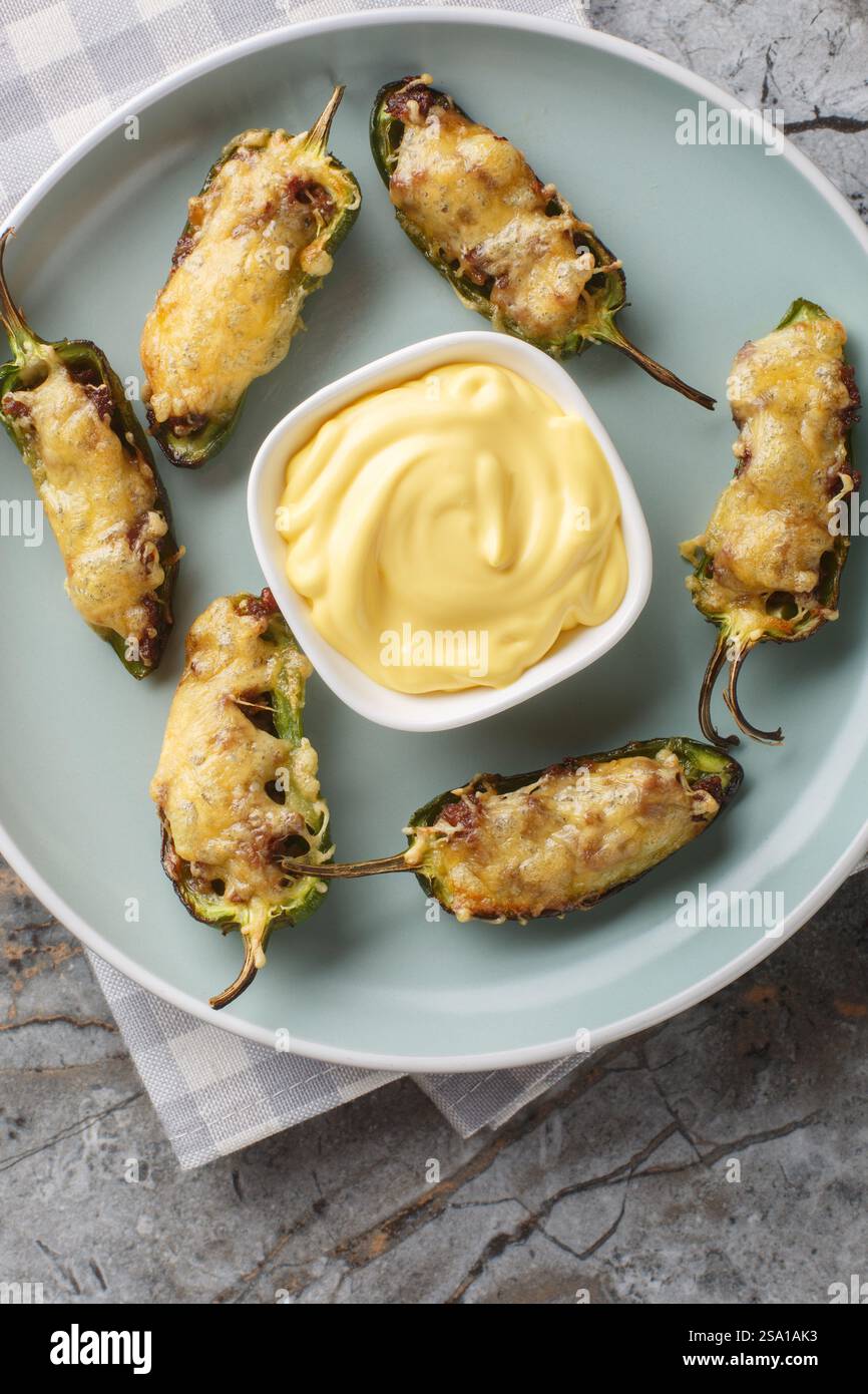 Poppers jalapeno bio faits maison avec viande hachée et fromage servi avec une sauce au fromage gros plan sur l'assiette sur la table. Vue de dessus verticale Banque D'Images