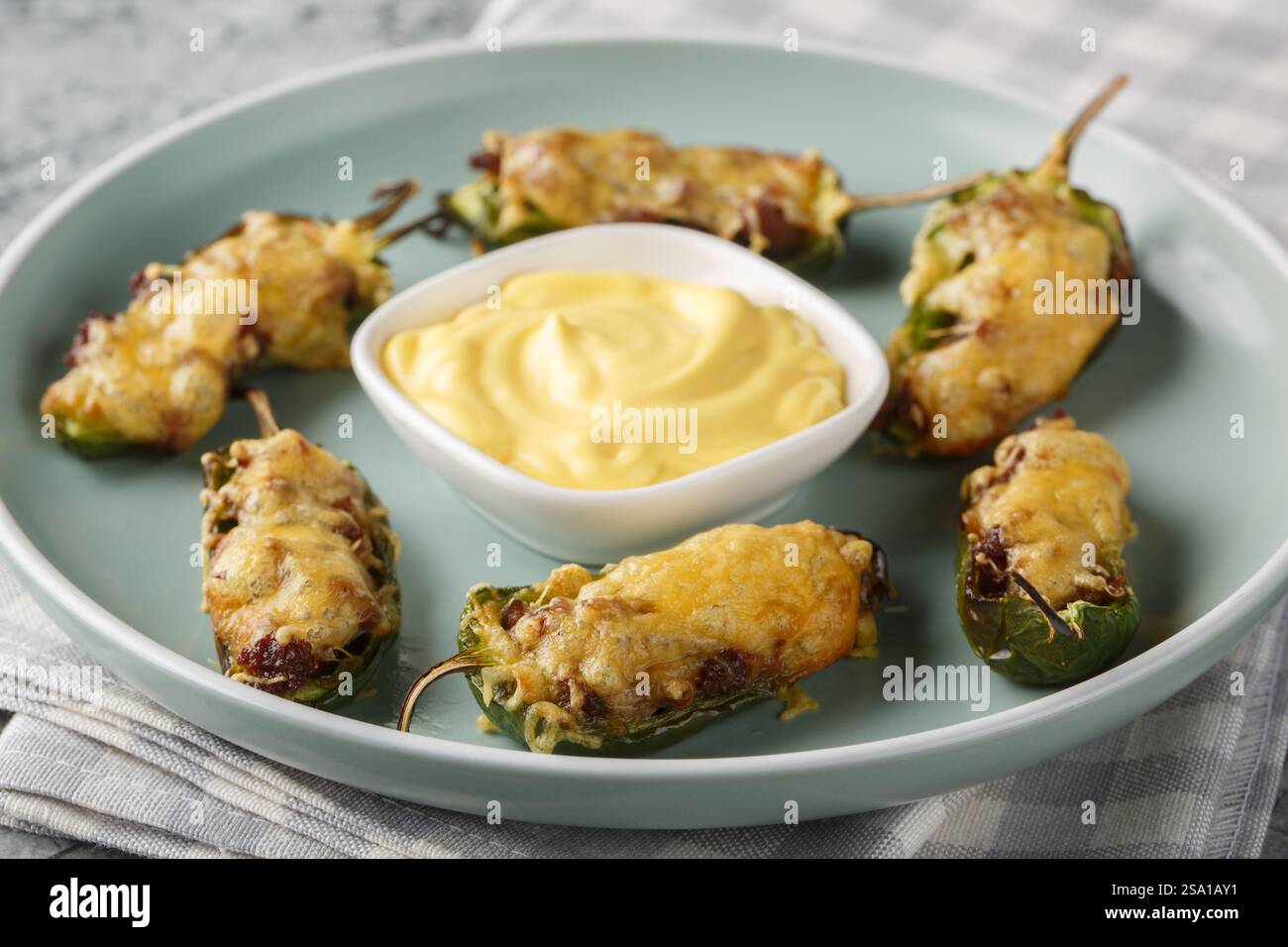 Poivrons jalapeno mexicains cuits au four avec du bœuf haché et du fromage servis avec une sauce de trempage gros plan dans une assiette sur une table. Horizontal Banque D'Images