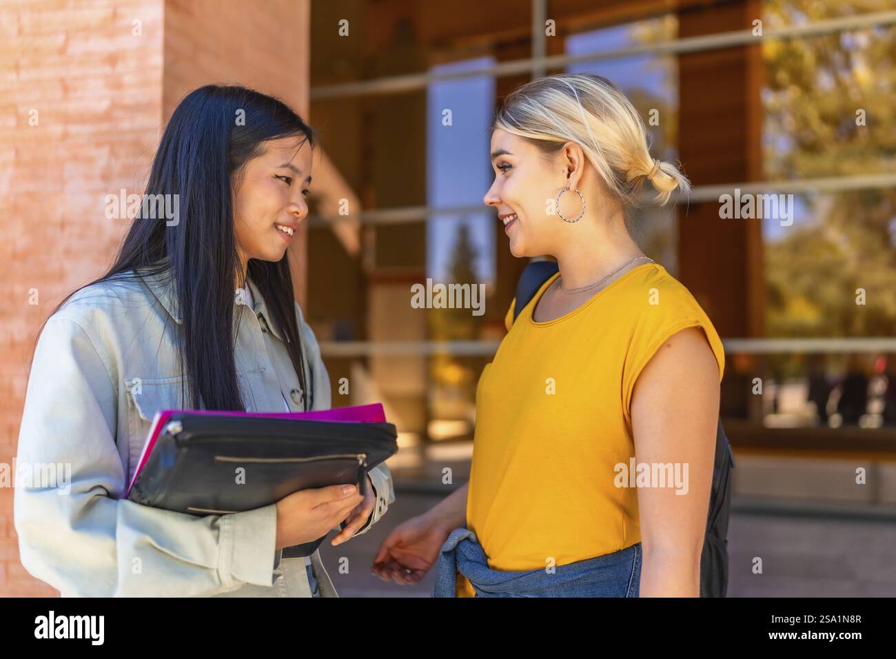 Deux étudiantes cauacsiennes et chinoises multiethniques discutant devant l'entrée de l'université Banque D'Images