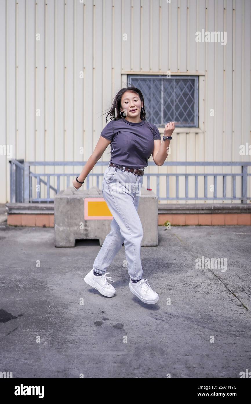 Photo verticale pleine longueur d'une jeune étudiante asiatique de beauté dansant k-pop à côté d'un bâtiment industriel Banque D'Images