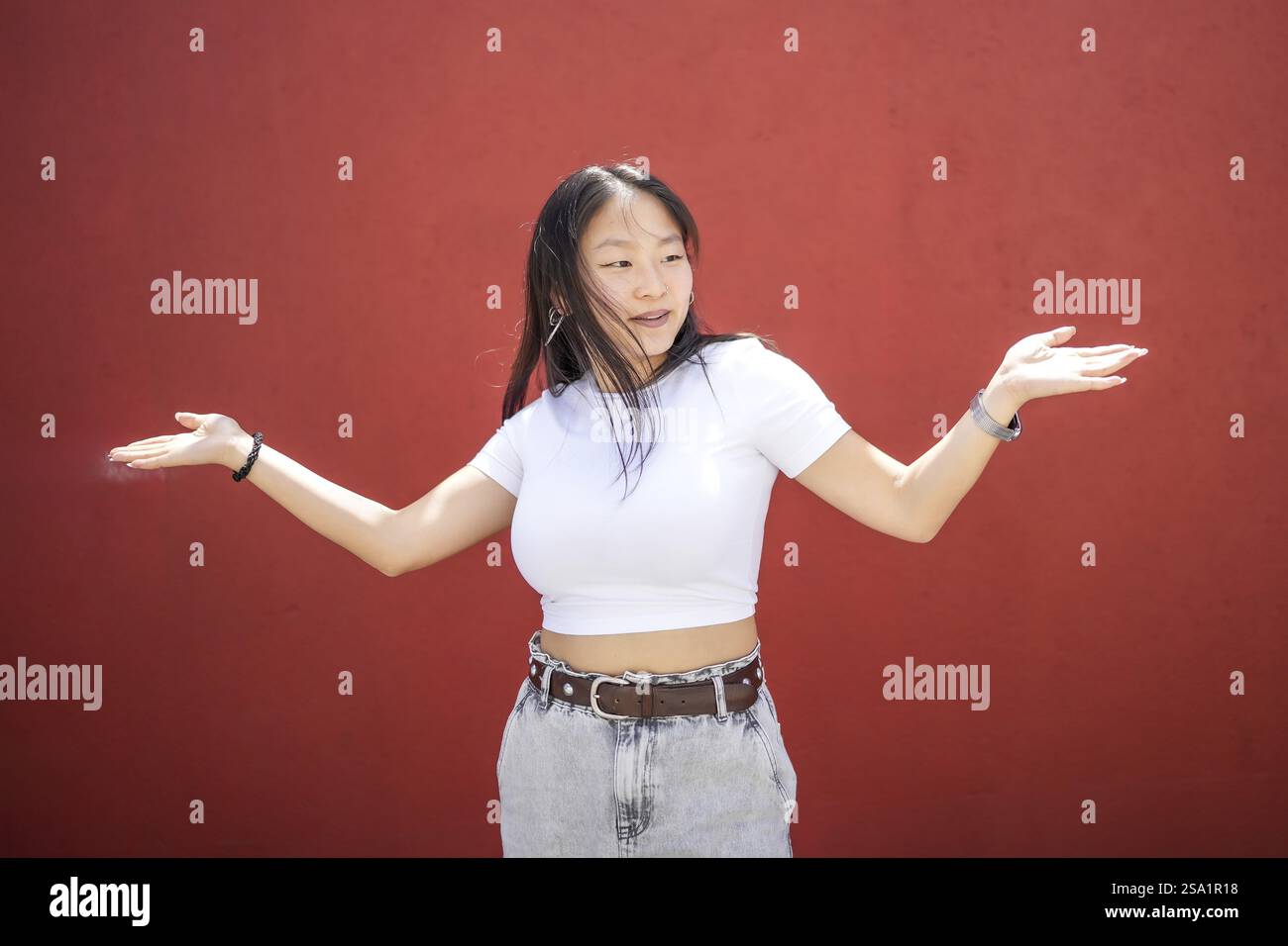 Jeune femme souriante asiatique agitant des mains dansant la danse urbaine K-pop contre un mur rouge urbain Banque D'Images