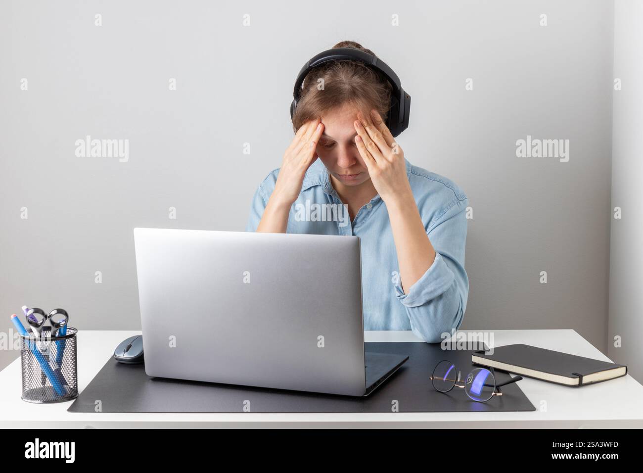 Une femme freelance surchargée de travail est fatiguée et stressée derrière son ordinateur portable. Problème d'épuisement et d'épuisement du travail à distance. La femme lutte avec fatigu Banque D'Images