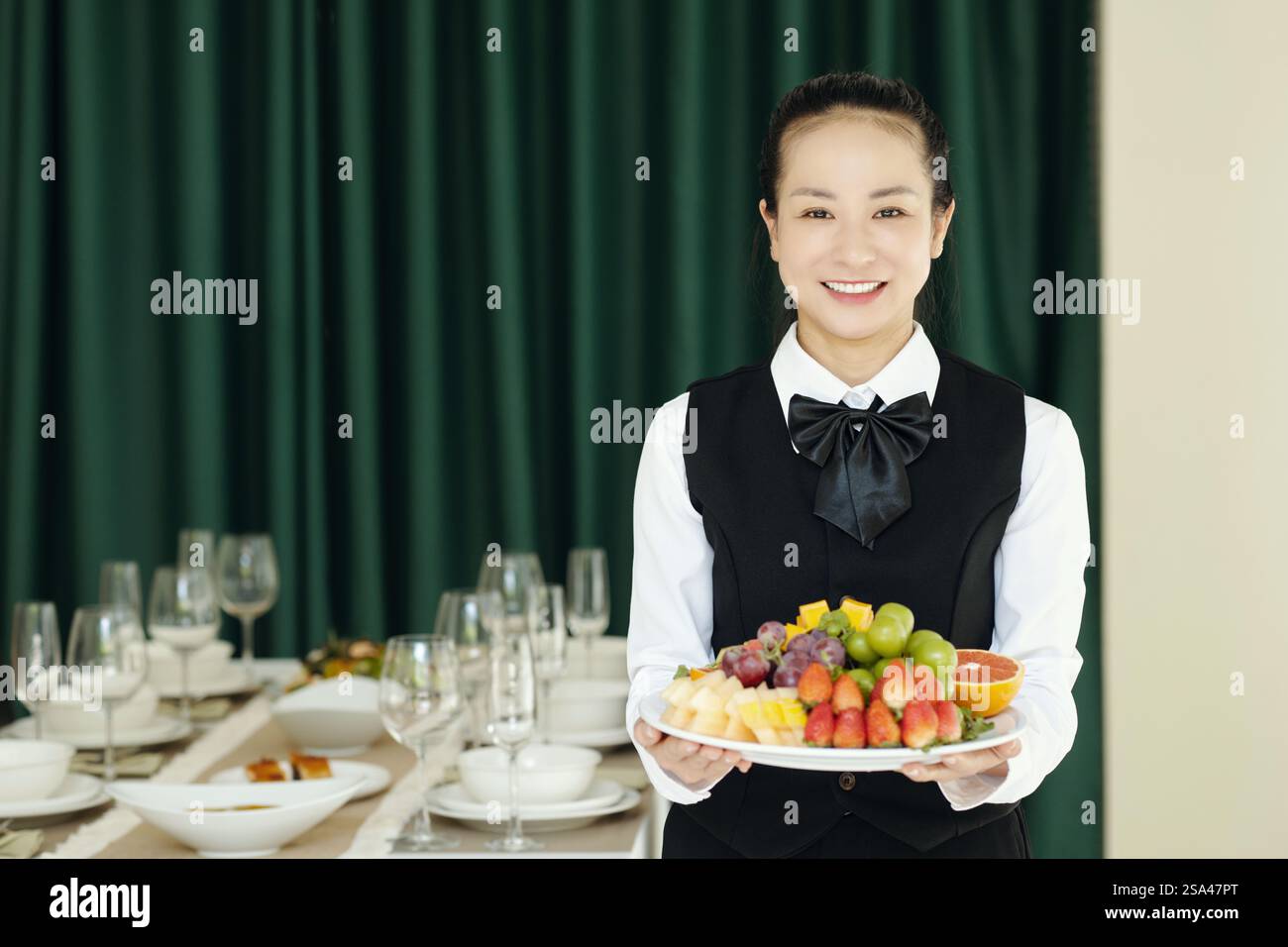 Portrait de jeune serveuse asiatique dans une assiette de maintien uniforme avec des fruits frais et les mettant sur la table Banque D'Images