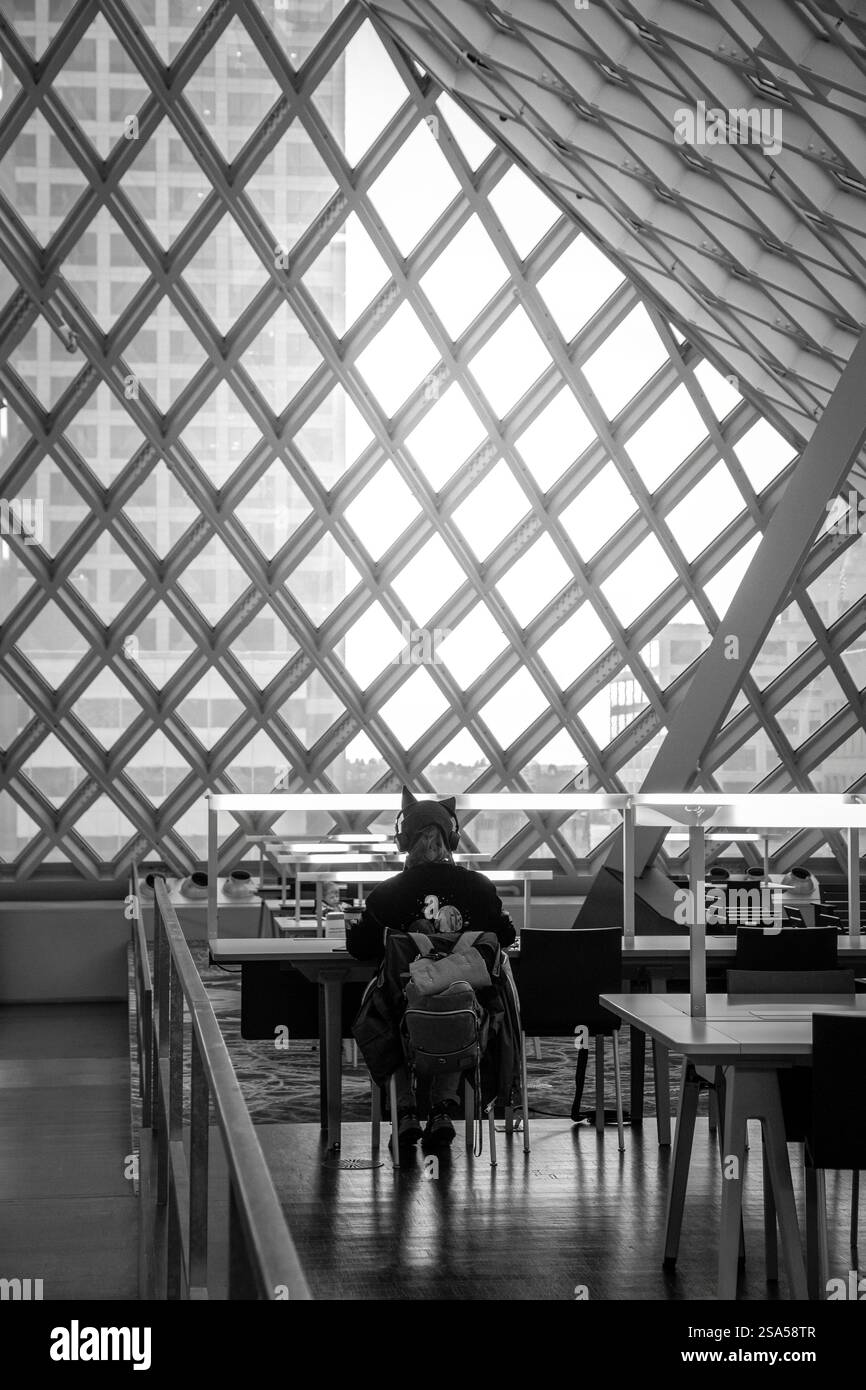 Une image en noir et blanc de l'intérieur de la bibliothèque publique de Seattle, mettant en évidence ses fenêtres géométriques emblématiques et une personne qui étudie tranquillement. Banque D'Images