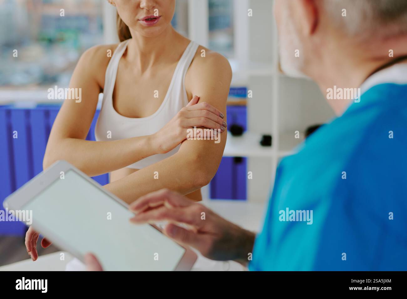 Au-dessus de l'épaule vue d'un médecin méconnaissable avec l'écoute de tablette se plaint oh son patient qui explique la peinture dans les biceps Banque D'Images