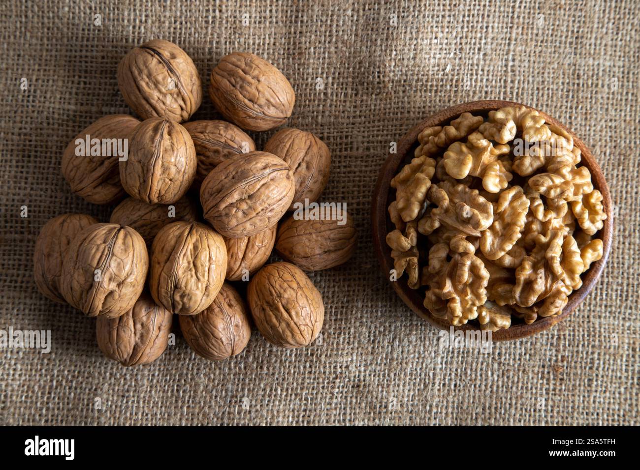 Un bol en bois rempli de cerneaux de noix, placé à côté des noix entières dans leurs coquilles sur toile de jute Banque D'Images