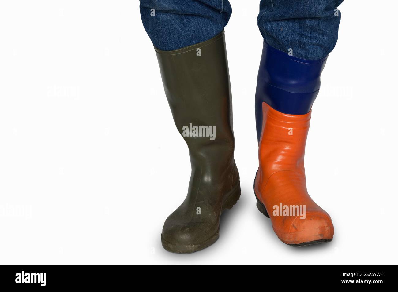 Un homme porte deux bottes en caoutchouc différentes, une verte pour les tâches générales et une botte de protection pour tronçonneuse pour travailler en toute sécurité avec des outils tranchants. Chaque botte est costume Banque D'Images