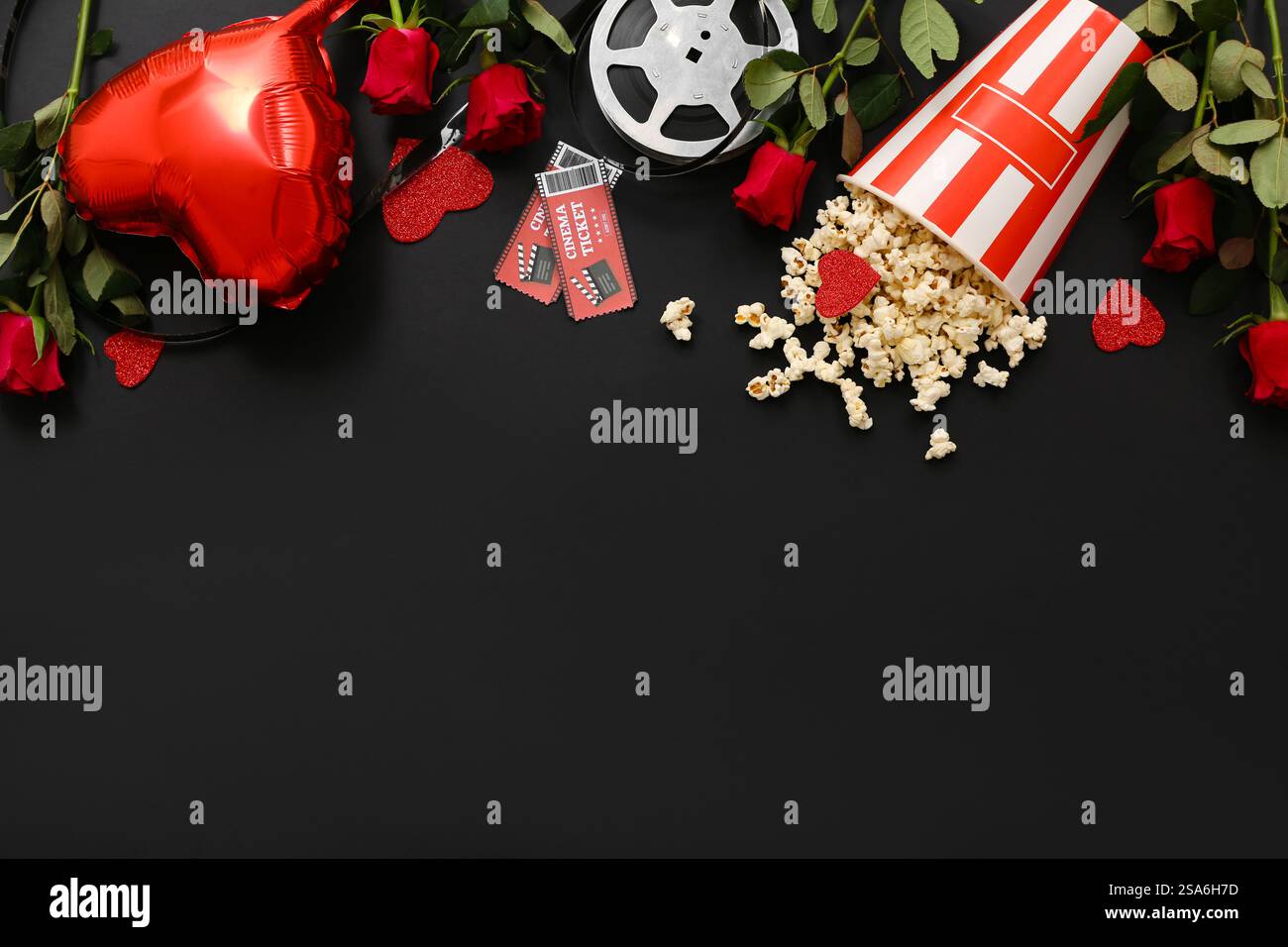 Seau de pop-corn avec billets de cinéma, bobine de film, roses rouges et ballon à air en forme de coeur sur fond noir. Célébration de la Saint-Valentin Banque D'Images