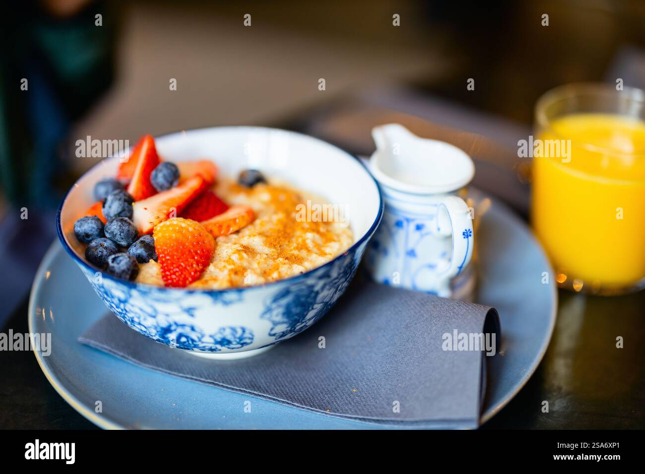 Un bol de flocons d'avoine crémeux garni de fraises fraîches, de bleuets et d'une pincée de cannelle, servi avec du lait et un verre de jus d'orange pour Banque D'Images