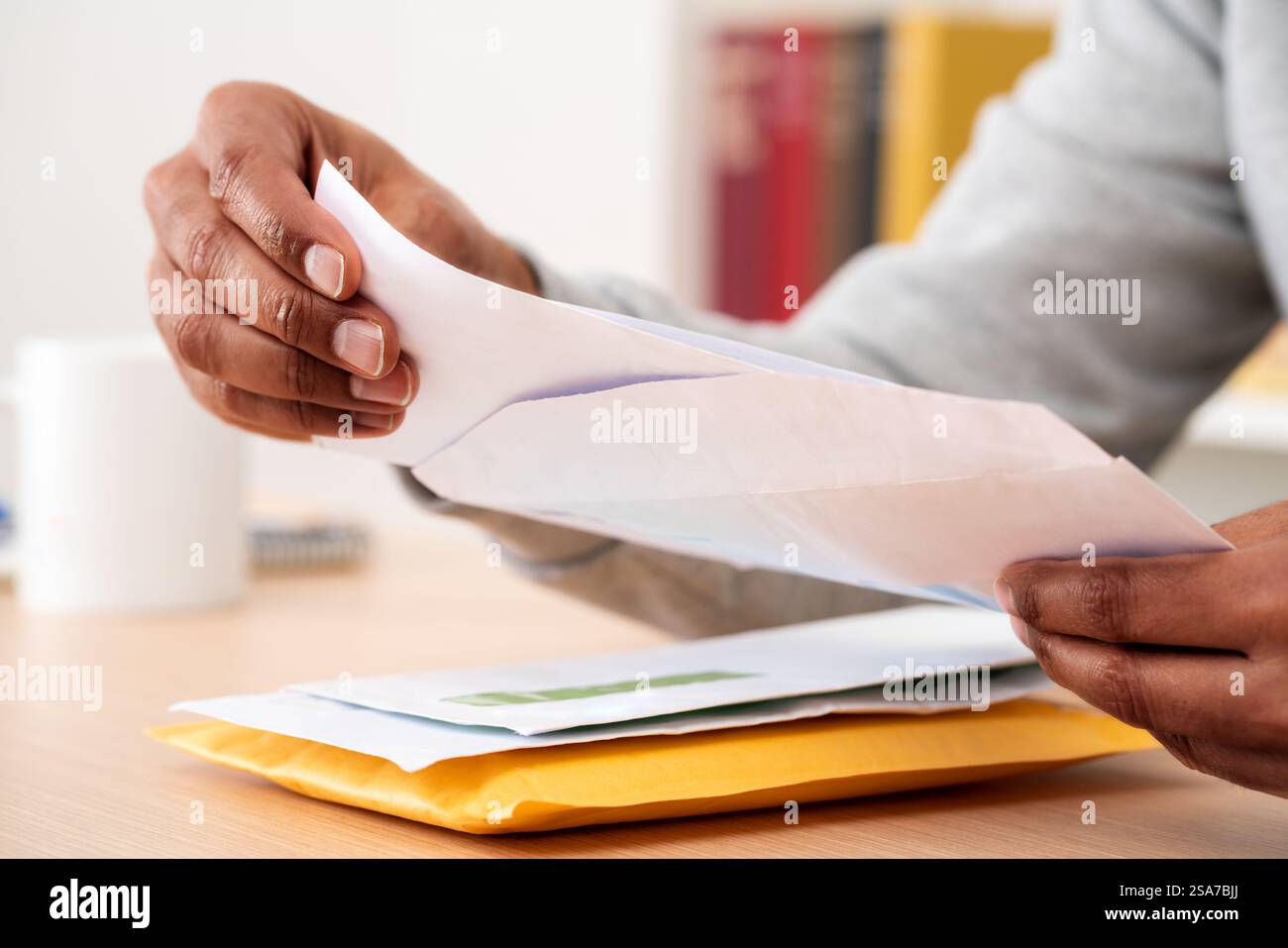 Gros plan de mains d'homme noir mettant une lettre à l'intérieur d'une enveloppe sur un bureau à la maison ou au bureau Banque D'Images