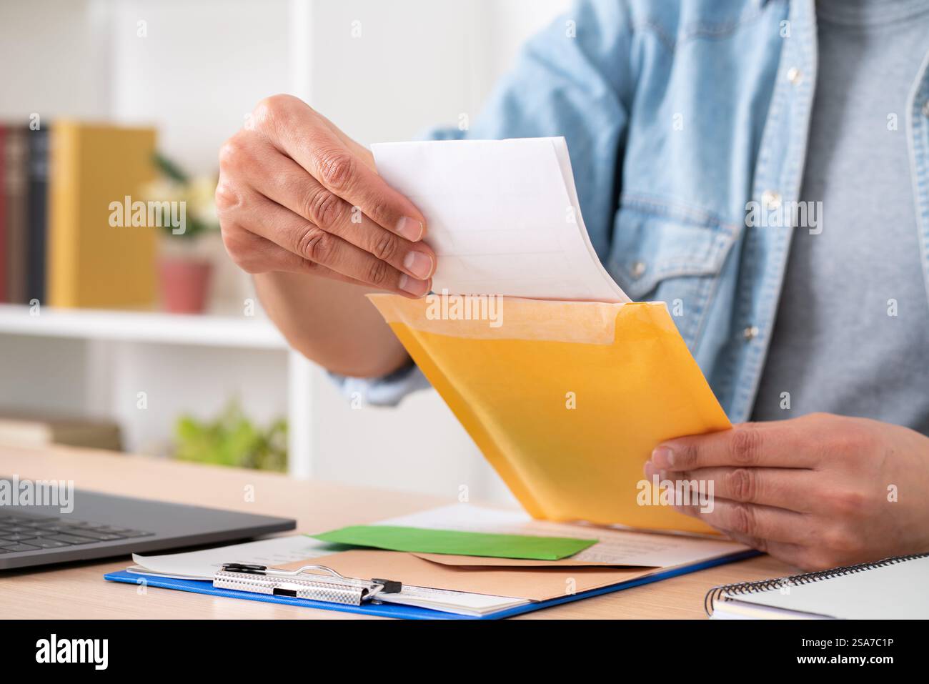 Gros plan des mains de l'homme ouvrant une lettre sur une enveloppe rembourrée sur un bureau à la maison Banque D'Images