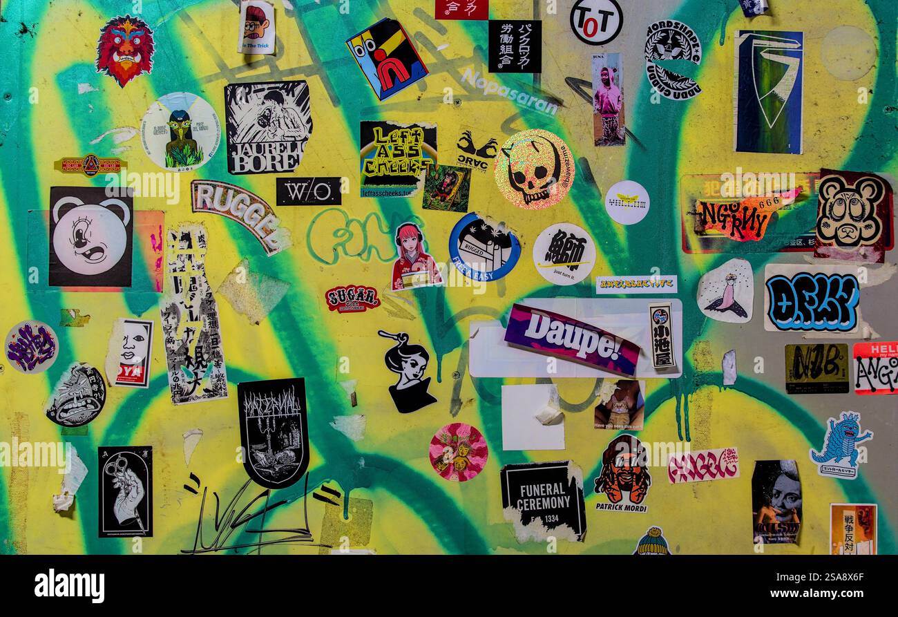 Vue rapprochée d'un mur couvert de graffitis verts et jaunes recouvert d'une variété éclectique d'autocollants Banque D'Images