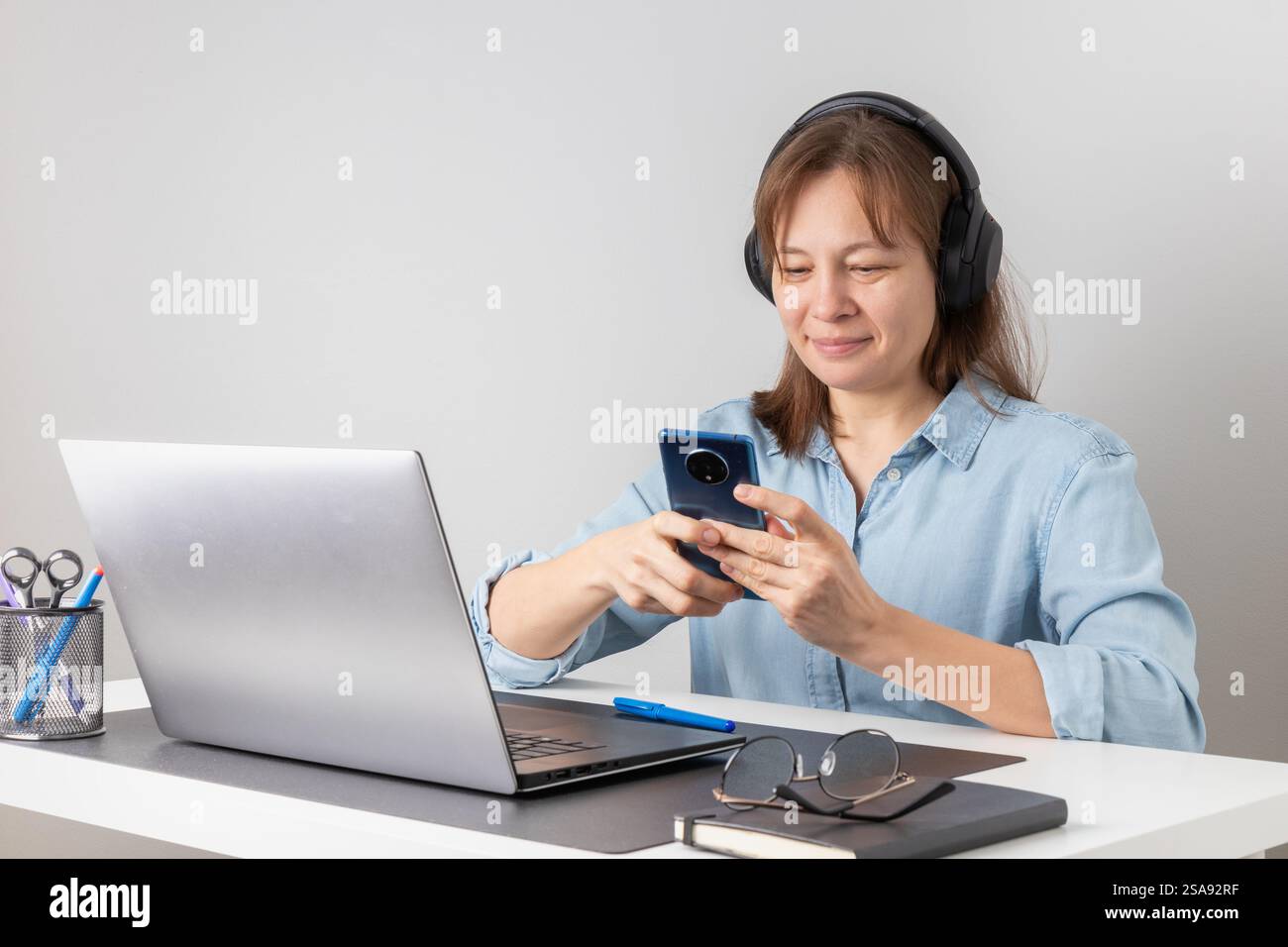 Jeune freelance heureuse, souriante jolie travailleuse professionnelle regardant smartphone, en utilisant la technologie mobile de téléphone portable travaillant à la maison ou moi Banque D'Images