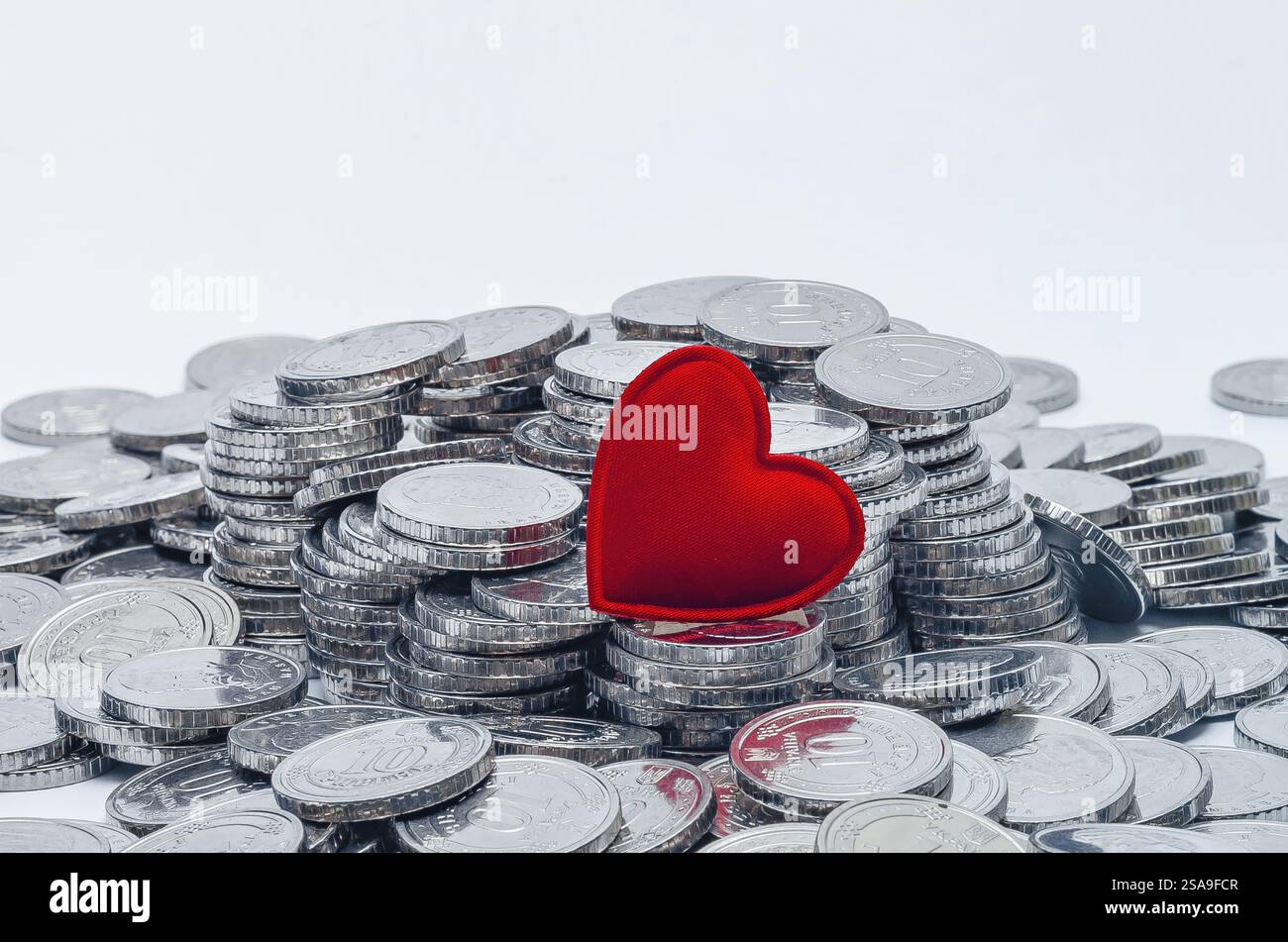 Un coeur rouge sur pile de pièces brillantes. Fond blanc. Carte de Saint-Valentin. Place pour l'inscription Banque D'Images