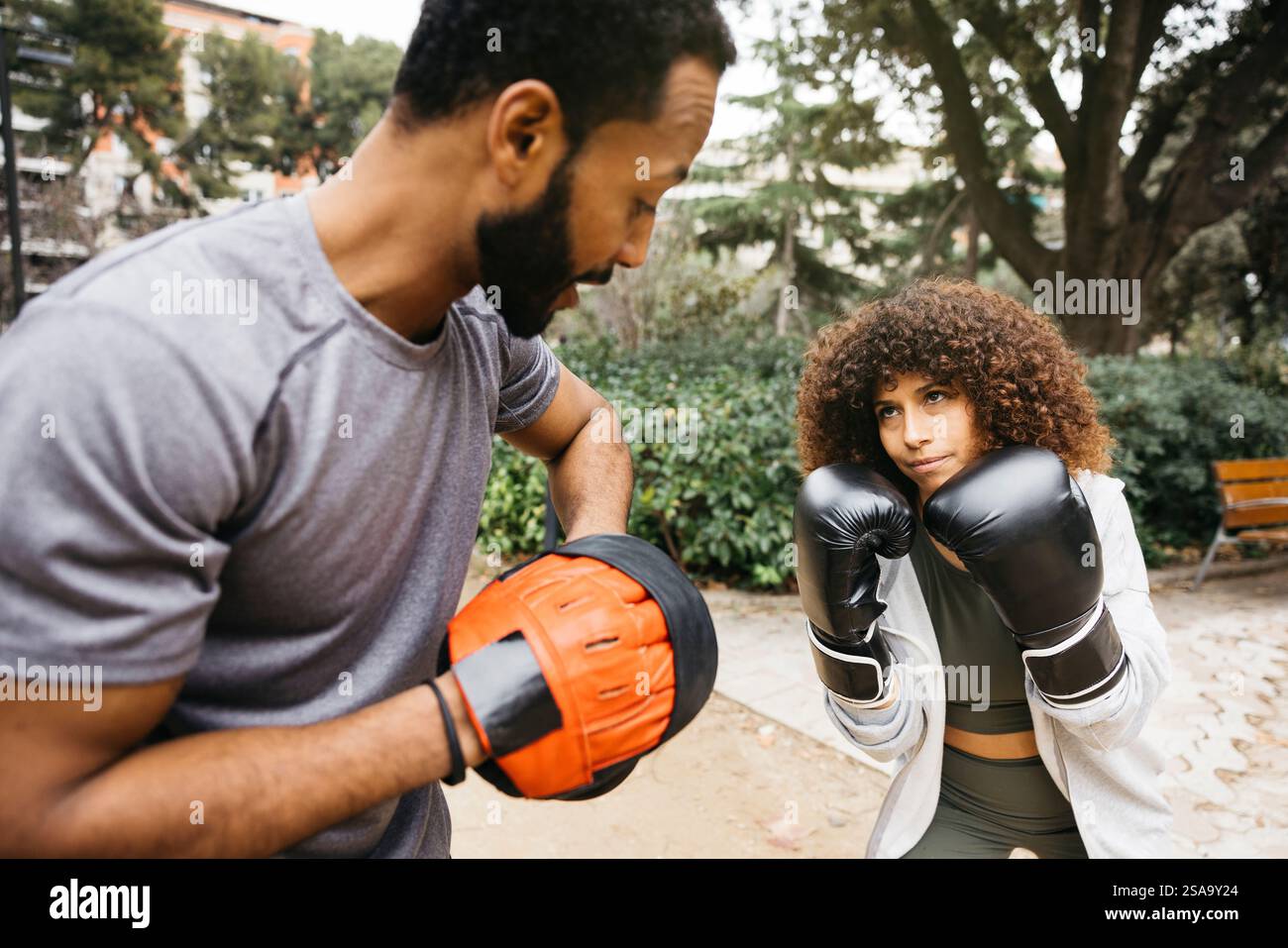 Un entraîneur de boxe instruisant une jeune femme dans un parc lors d'une séance d'entraînement, mettant l'accent sur la forme physique et la technique de boxe. Banque D'Images