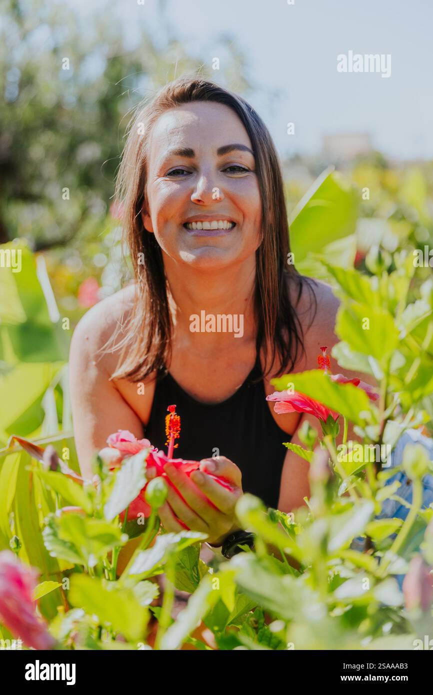 Une femme sourit et tient une fleur rose dans sa main. Concept de bonheur et de contentement, comme la femme profite de la beauté de la fleur et Banque D'Images