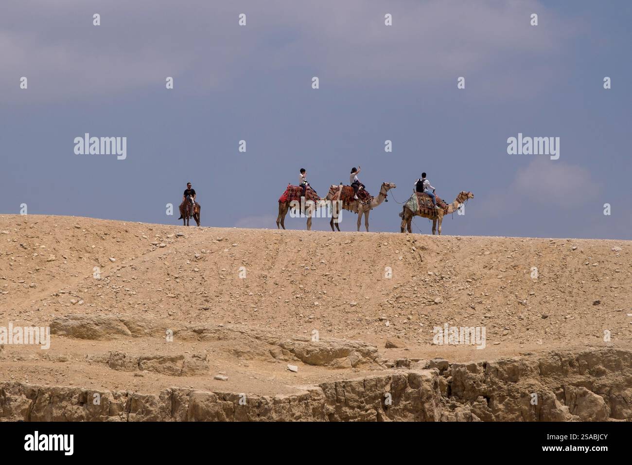Paysage désertique avec des touristes sur des chameaux visitant la plaine de Gizeh Banque D'Images