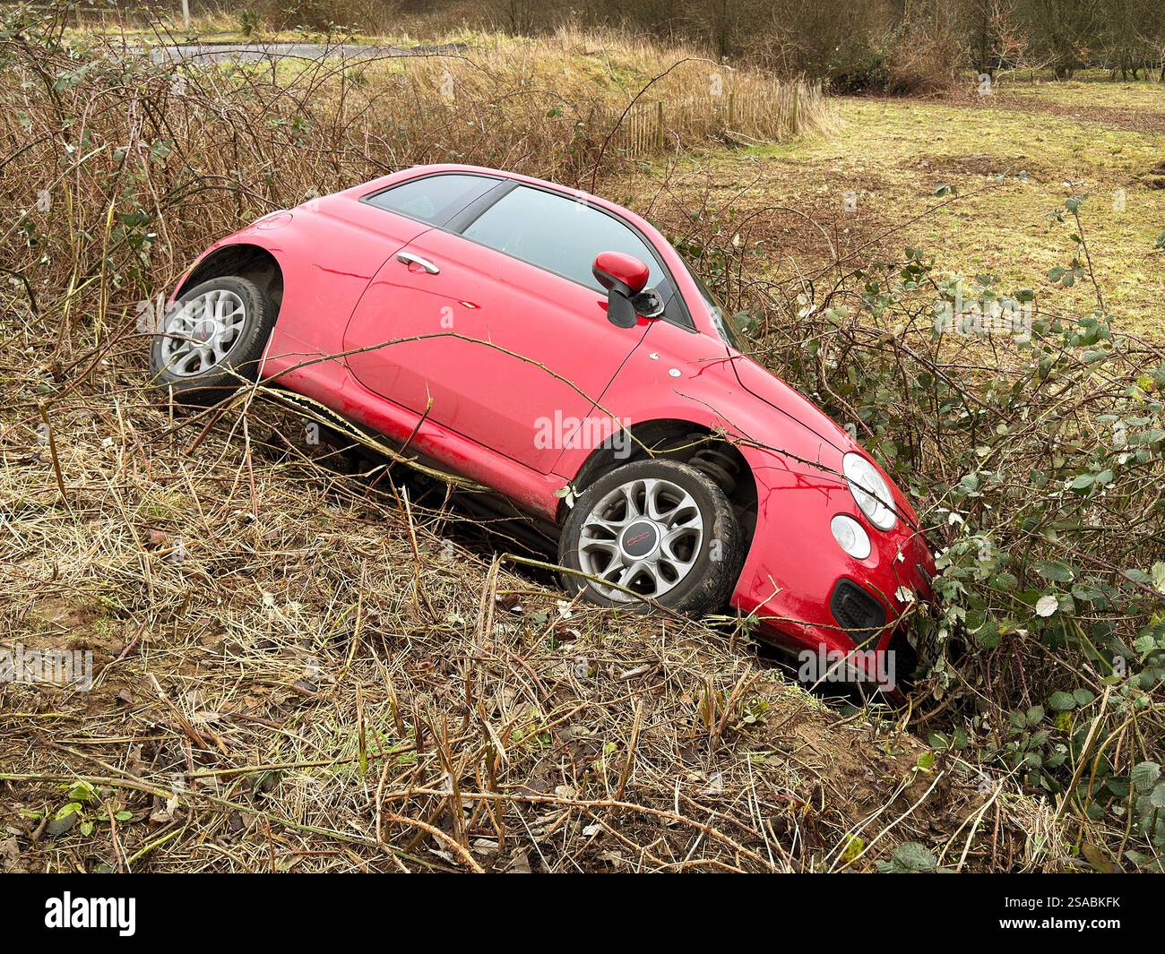 Pontyclun, pays de Galles, Royaume-Uni - 29 janvier 2025 : petite voiture rouge sur le côté dans les buissons après s'être écrasée sur une route. Personne. Banque D'Images