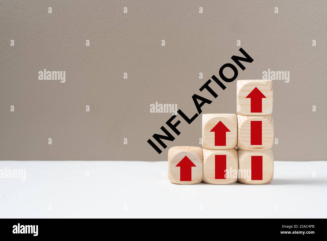 Une représentation visuelle de l'inflation utilisant des blocs de bois avec des flèches rouges vers le haut empilées pour représenter l'augmentation des coûts, avec le mot INFLATION Banque D'Images