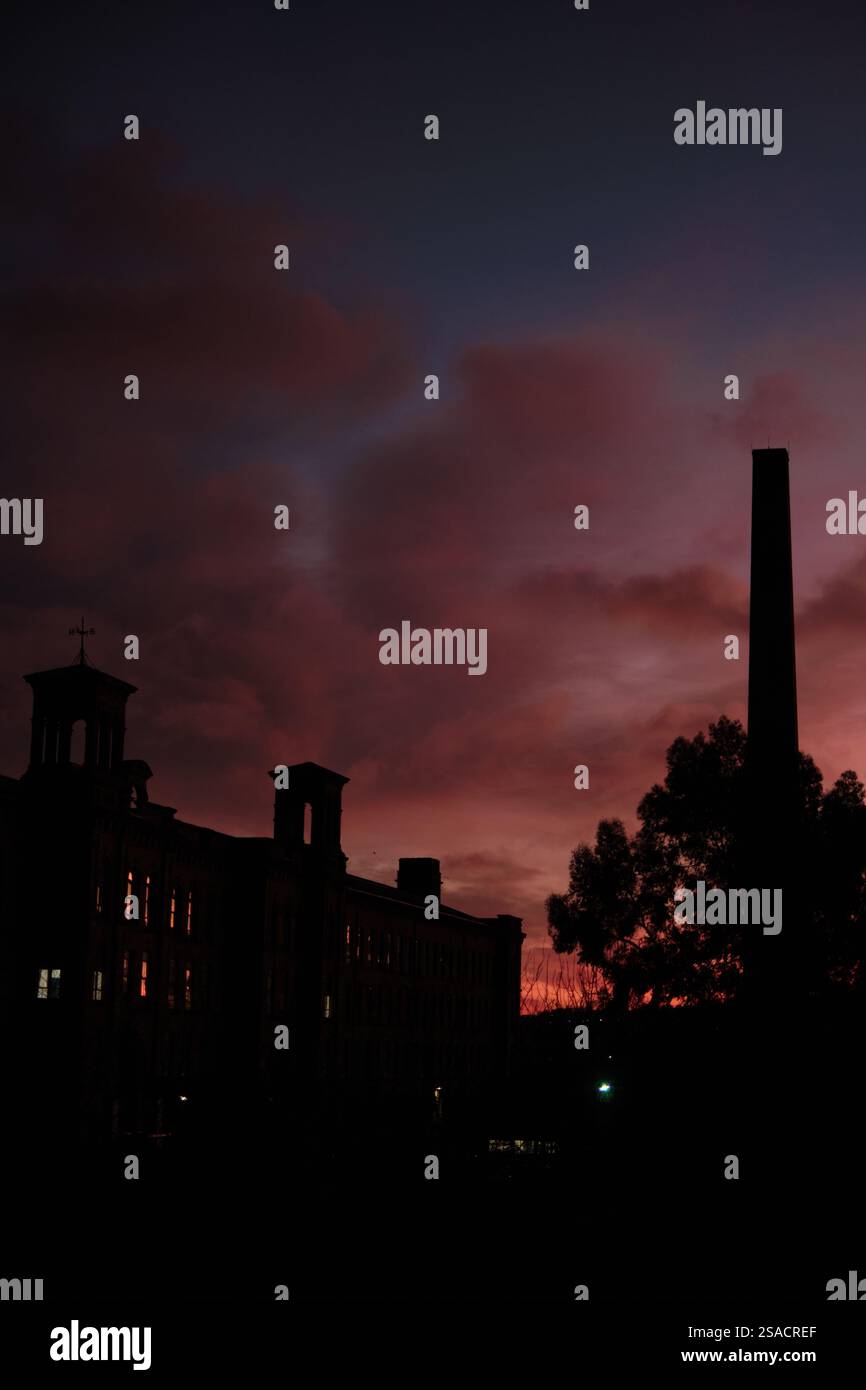 Ciel rouge spectaculaire à l'aube sur Salts Mill, une usine de textile vactorien dans le village de Saltaire, site classé au patrimoine mondial de l'UNESCO, Shipley près de Bradford, Yorkshire. Banque D'Images