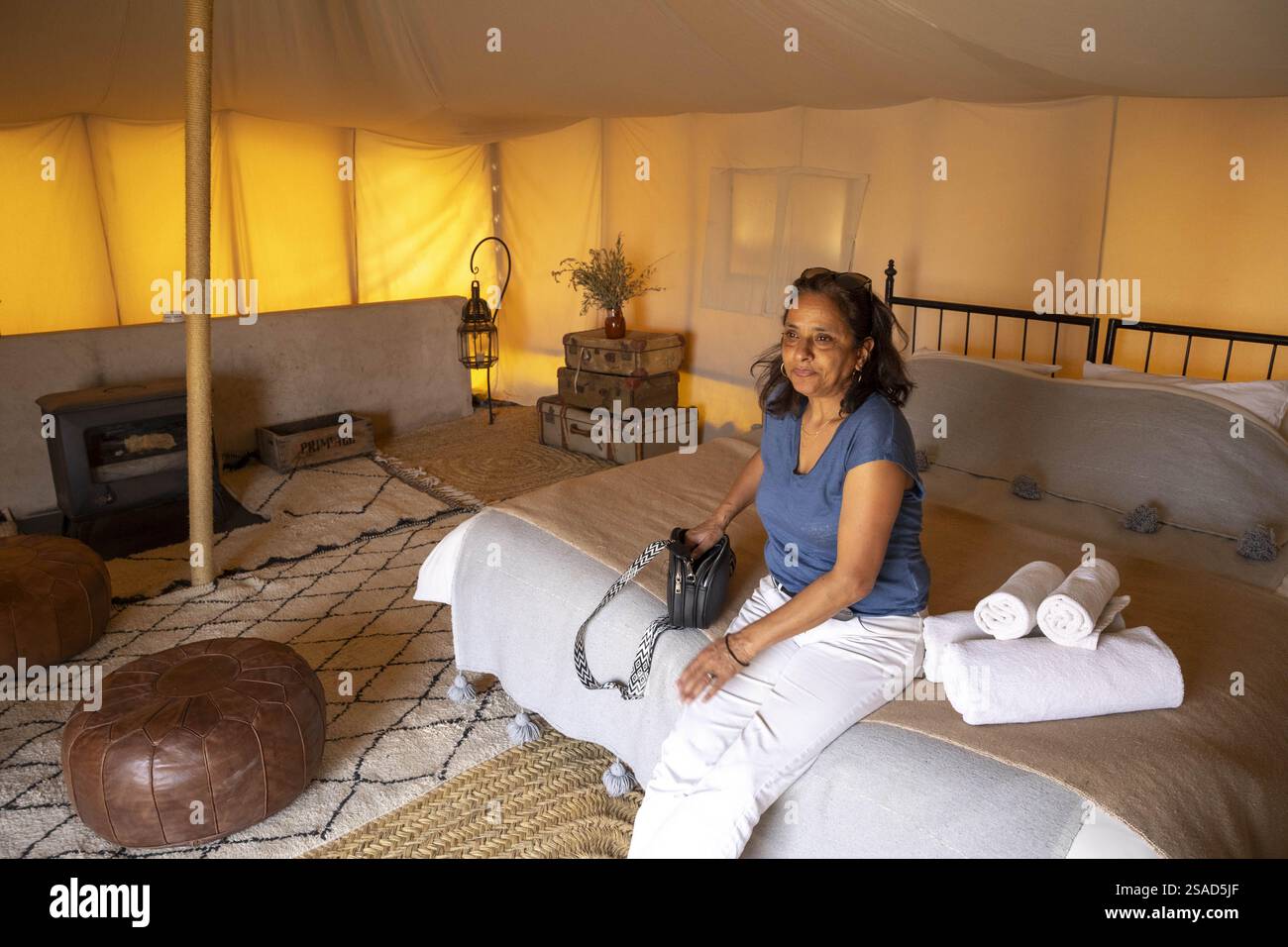 Touriste assis sur un lit dans un camp de luxe dans le désert d'Agafay, Maroc Banque D'Images Touriste assis sur un lit dans un camp de luxe dans le désert d'Agafay, Maroc Banque D'Images
