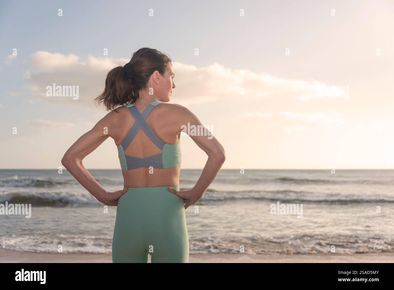 vue arrière d'une femme sportive en forme debout sur une plage regardant vers la mer se reposant après l'entraînement Banque D'Images vue arrière d'une femme sportive en forme debout sur une plage regardant vers la mer se reposant après l'entraînement Banque D'Images