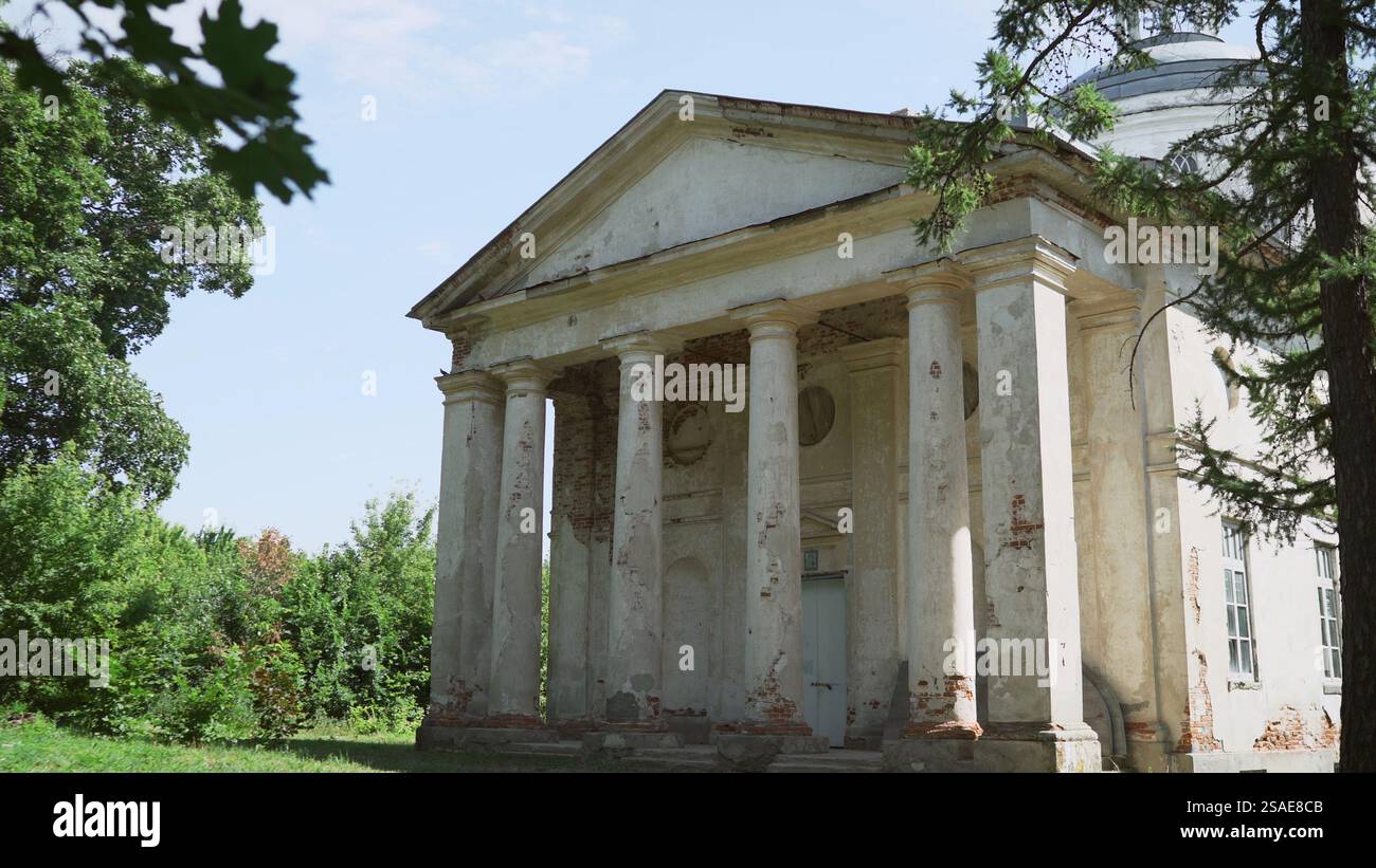 Majestueuse église blanche avec des colonnes proéminentes et un toit en dôme, montrant des signes de décomposition au milieu d'un cadre naturel verdoyant Banque D'Images