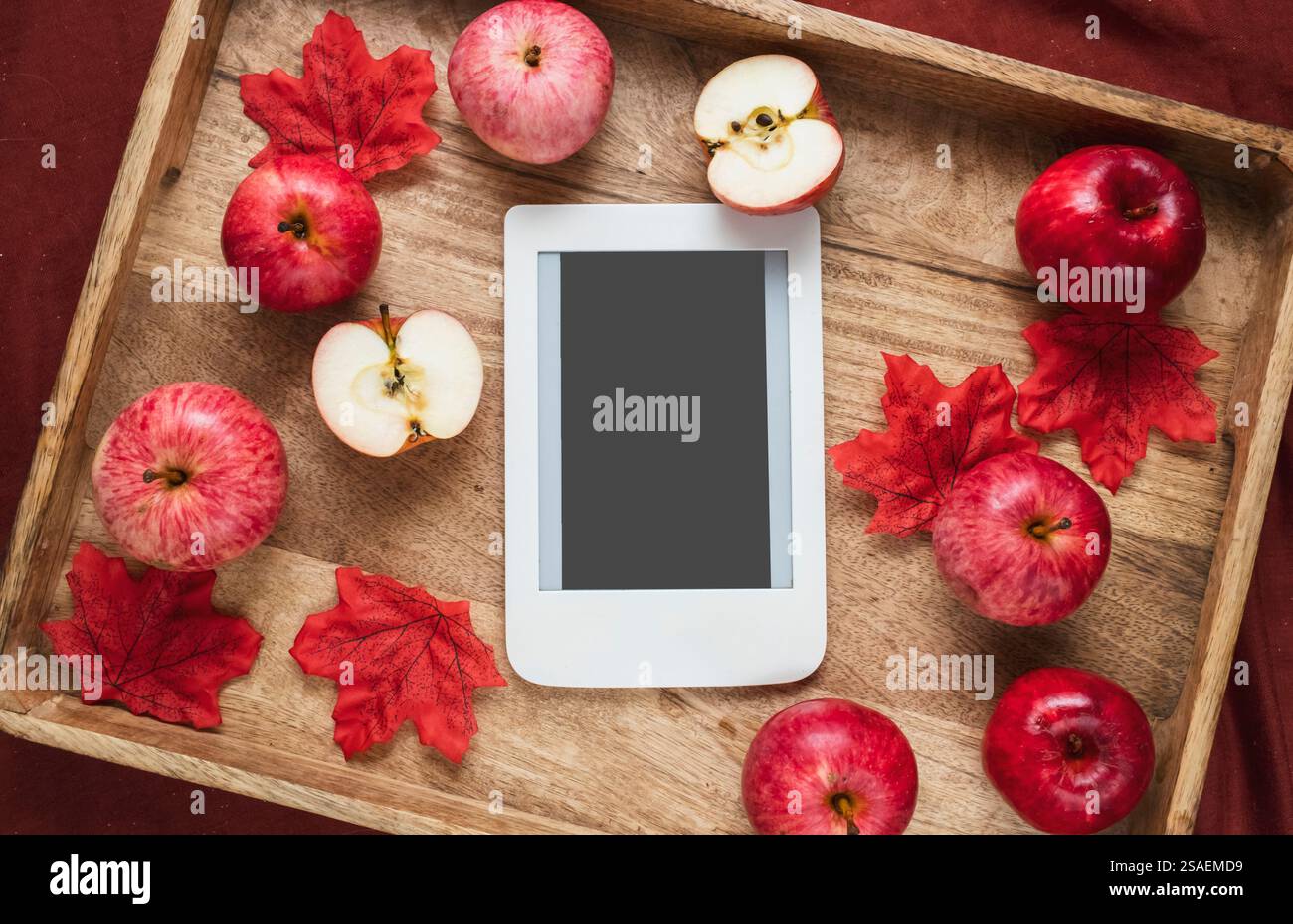 Maison d'automne composition confortable avec des feuilles rouges, des pommes rouges et e-book avec espace de copie sur plateau en bois. Saison d'automne. Banque D'Images