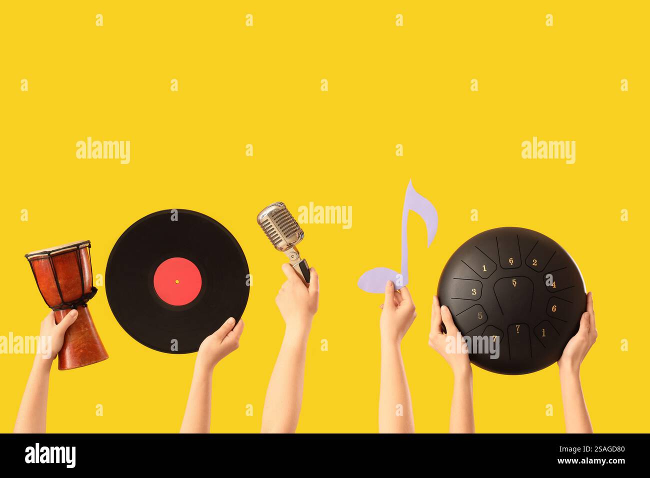 Mains féminines tenant tambour avec vinyle, microphone et glucophone sur fond jaune Banque D'Images