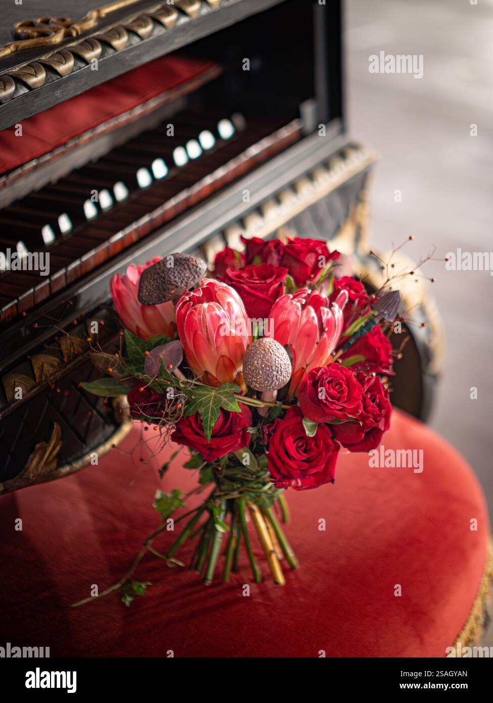 Élégant bouquet de mariage avec des roses rouges et des fleurs exotiques Protea sur Piano Vintage orné Banque D'Images