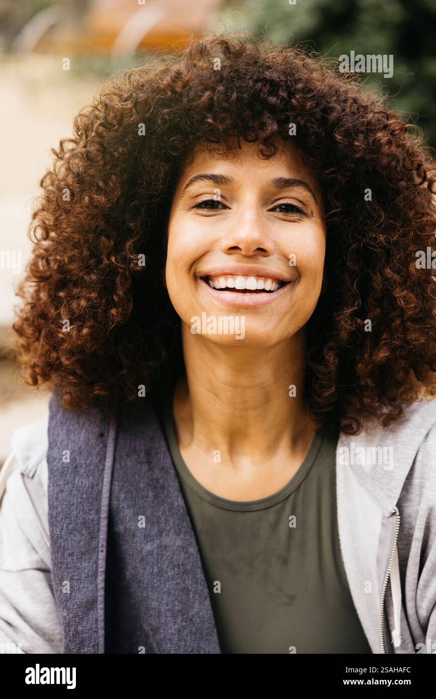Un portrait joyeux mettant en vedette une femme au sourire vif et aux cheveux bouclés profitant d'un moment post-exercice en plein air. Banque D'Images